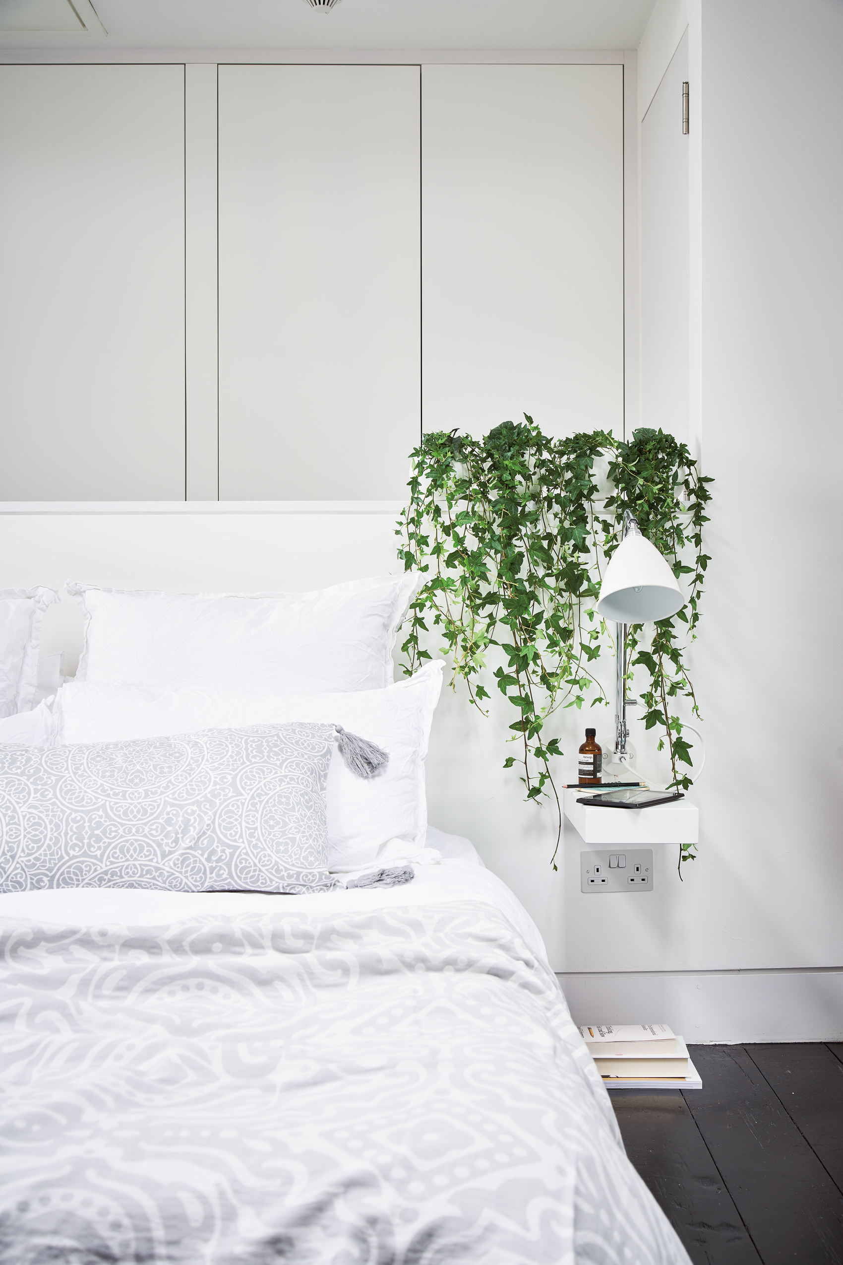 A line up of tiny, trailing Hedera helix (English ivy) hanging down from pots grouped on the bed head, turns a plain bedside shelf into a striking design statement. Room featured At Home With Plants (Nick Pope/Mitchell Beazley/PA)