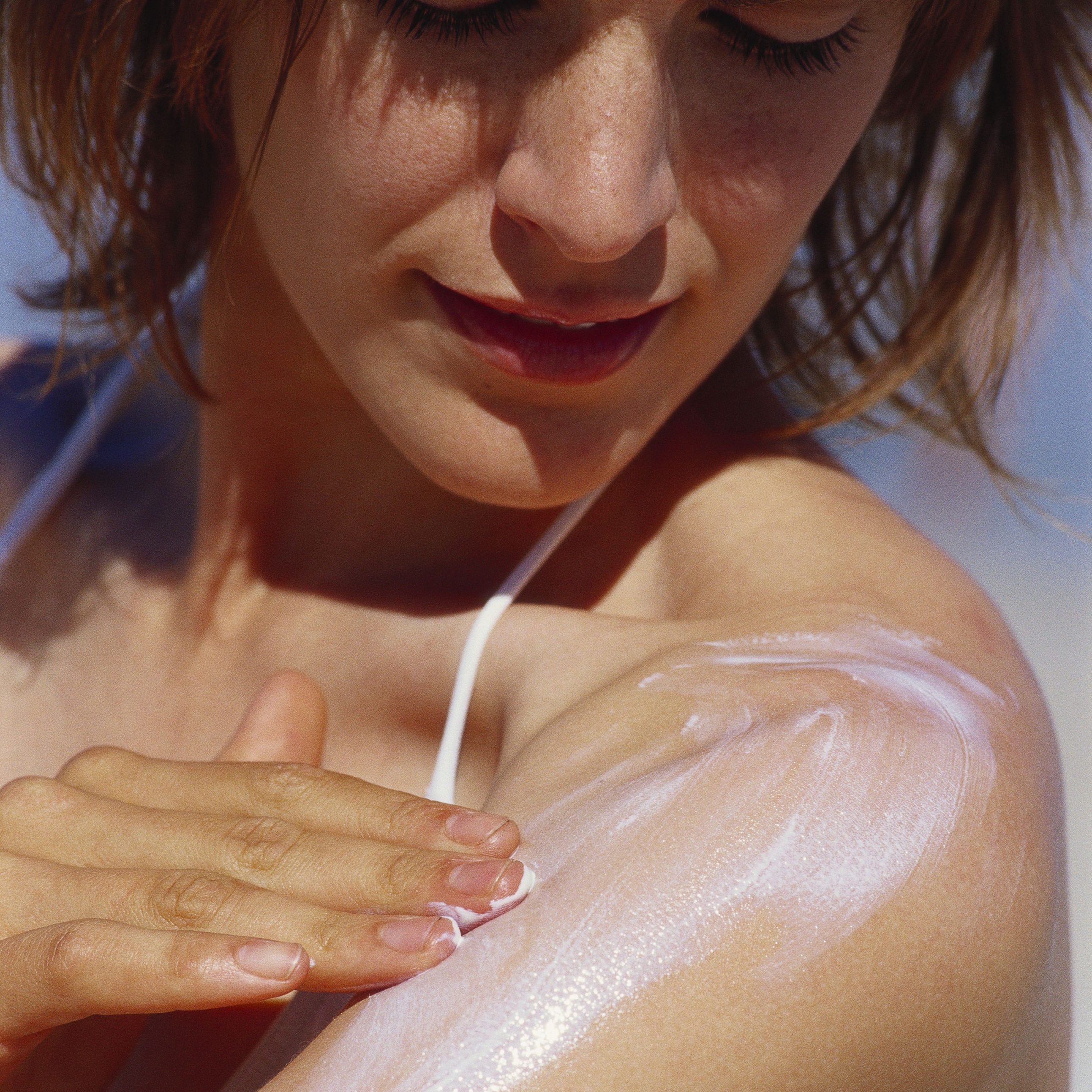 A woman applying sunscreen to her shoulder