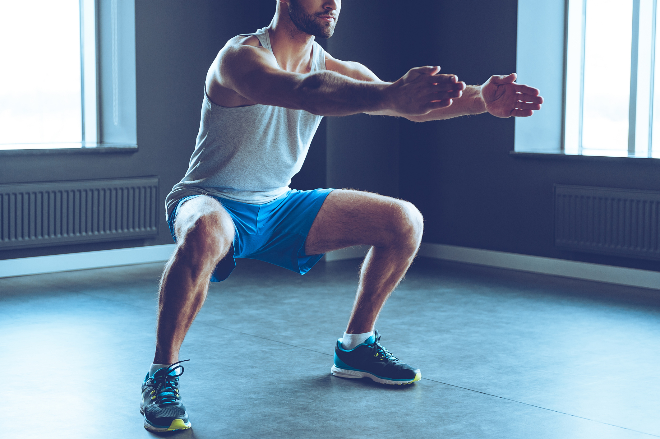 Part of young man in sportswear doing squat at gym