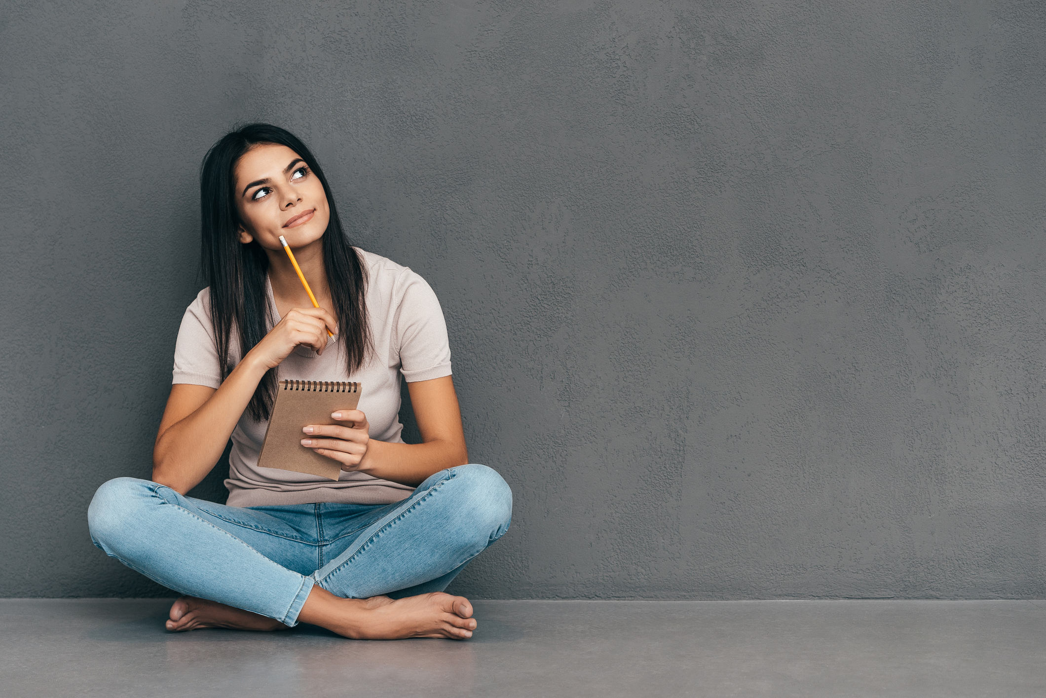 Attractive young woman in casual wear holding notebook and pen while sitting barefoot and against grey background (Thinkstock/PA)