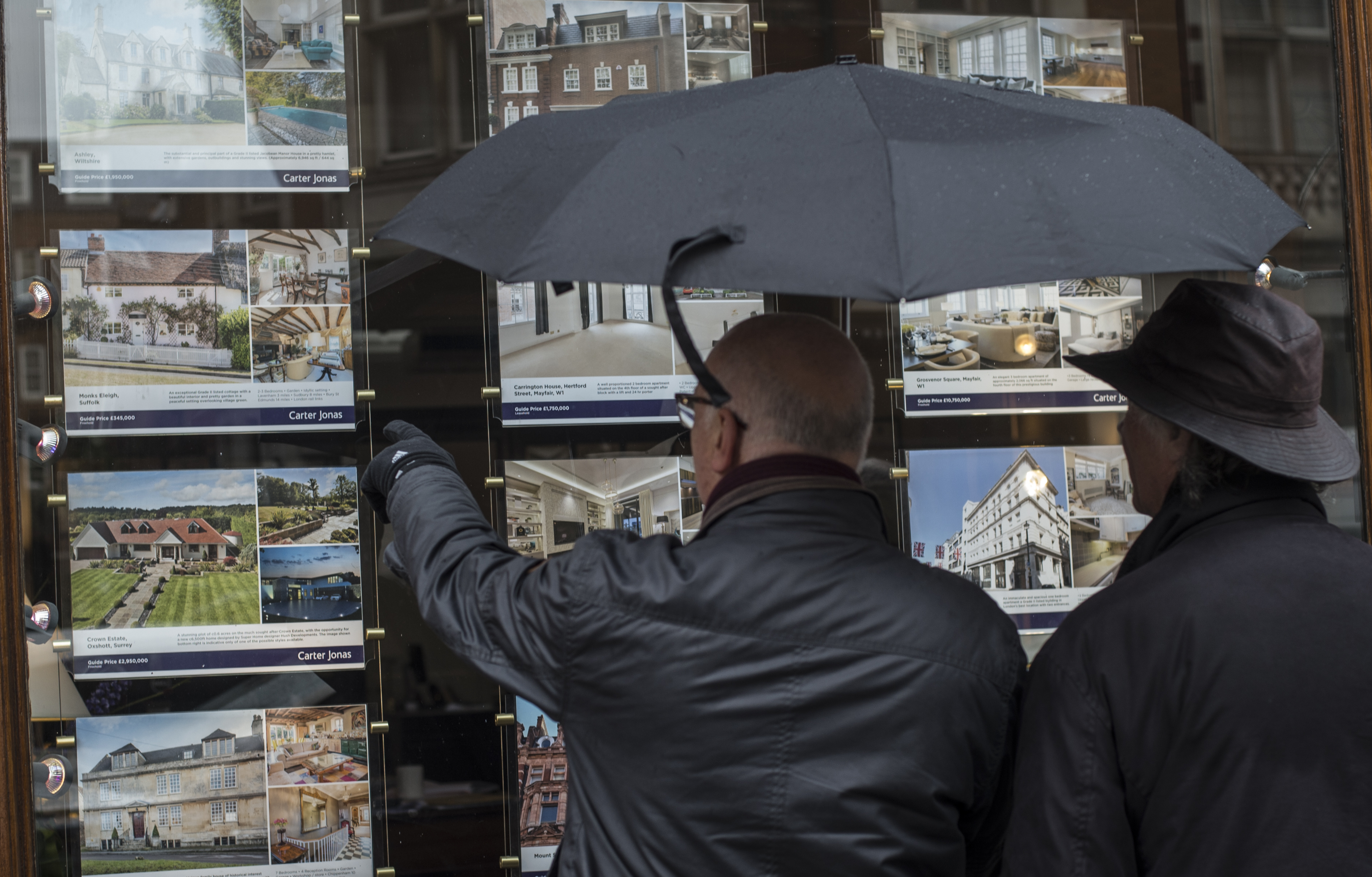 People look at houses for sale in the window of an estate agents in Mayfair, London