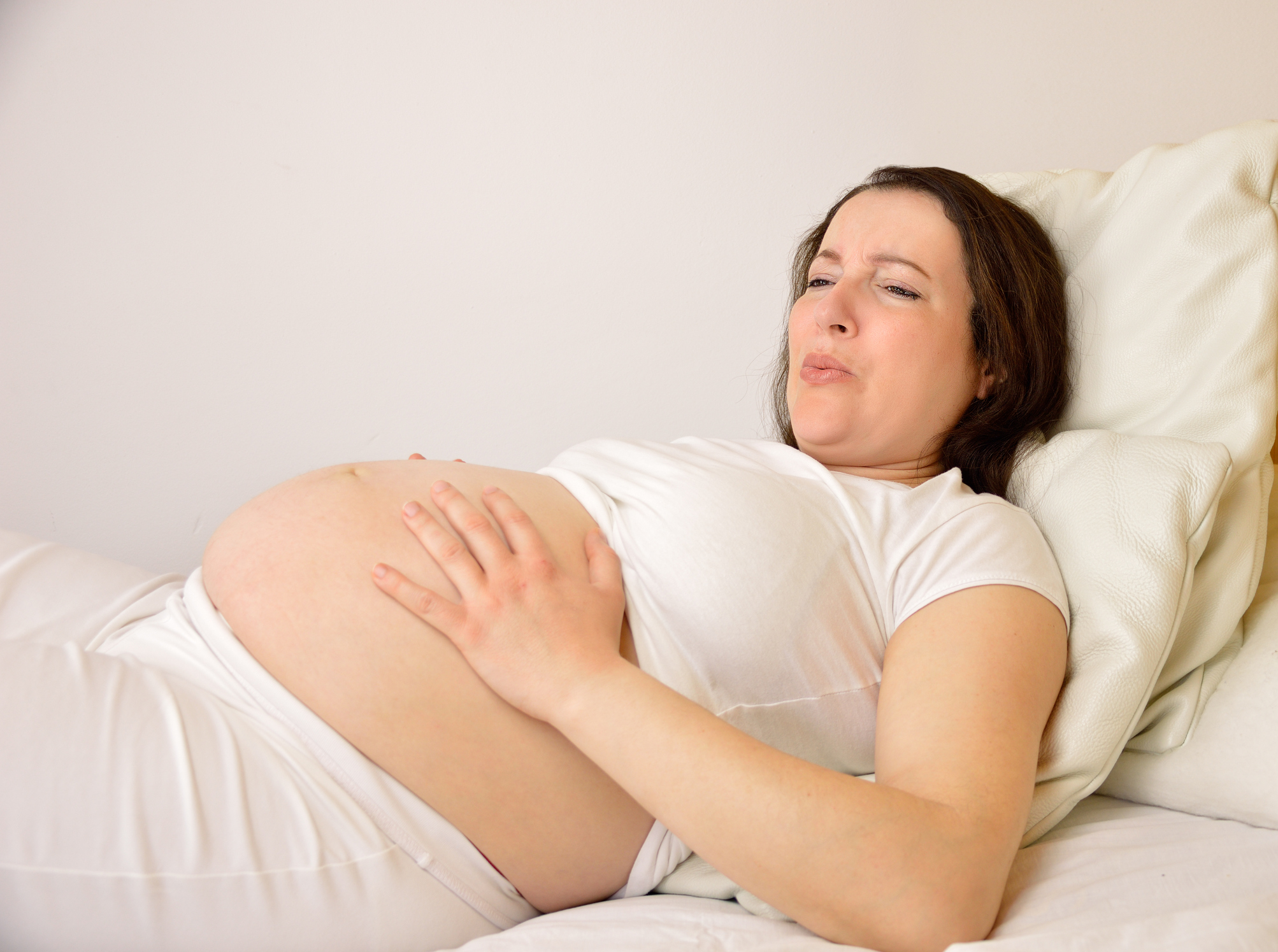 Pregnant woman suffering tummy ache lying on a bed at home (Thinkstock/PA)