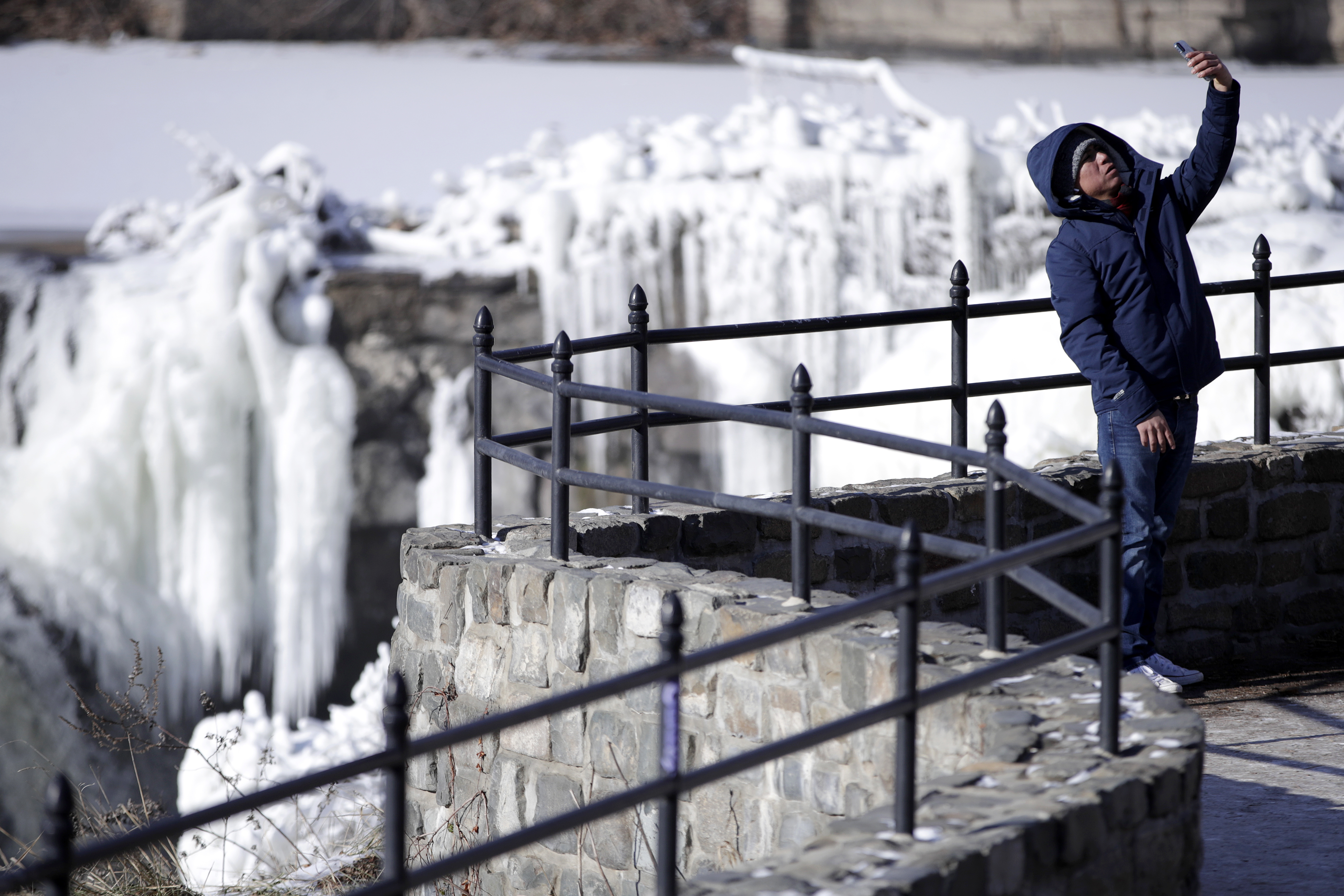 A tourist uses a mobile phone to capture a selfie in front of the partially frozen falls at the Paterson Great Falls National Historical Park