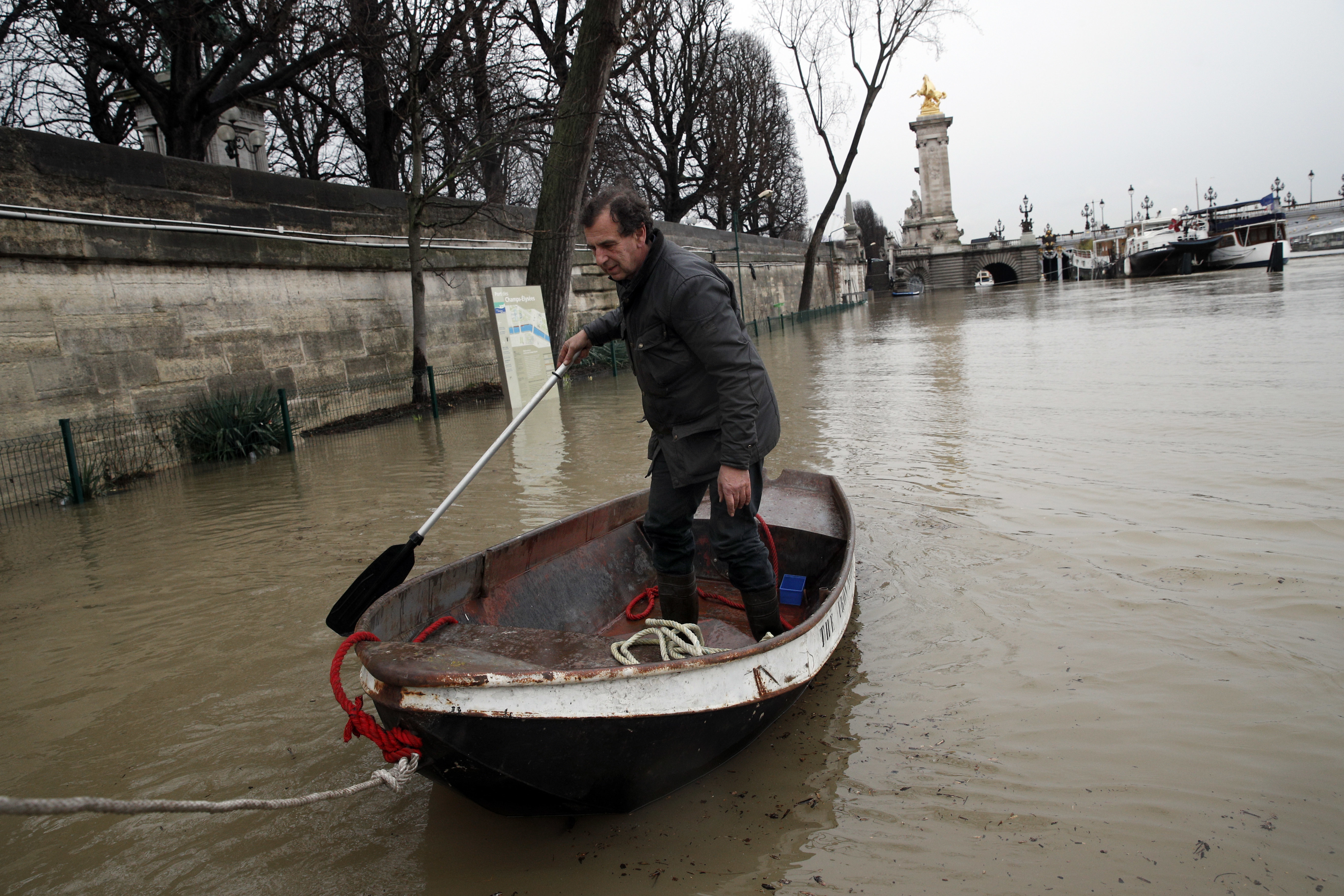 A man uses a dinghy boat to reach his barge on the river Seine in Paris (Christophe Ena/AP)