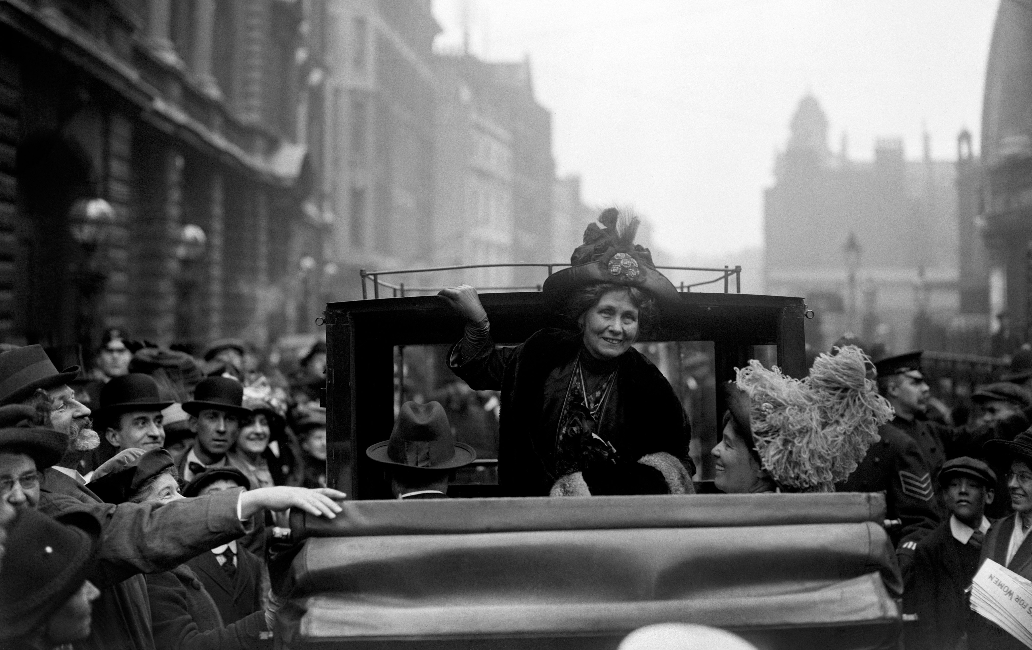 Woman smiling from the back of a carriage, with crowds of onlookers 