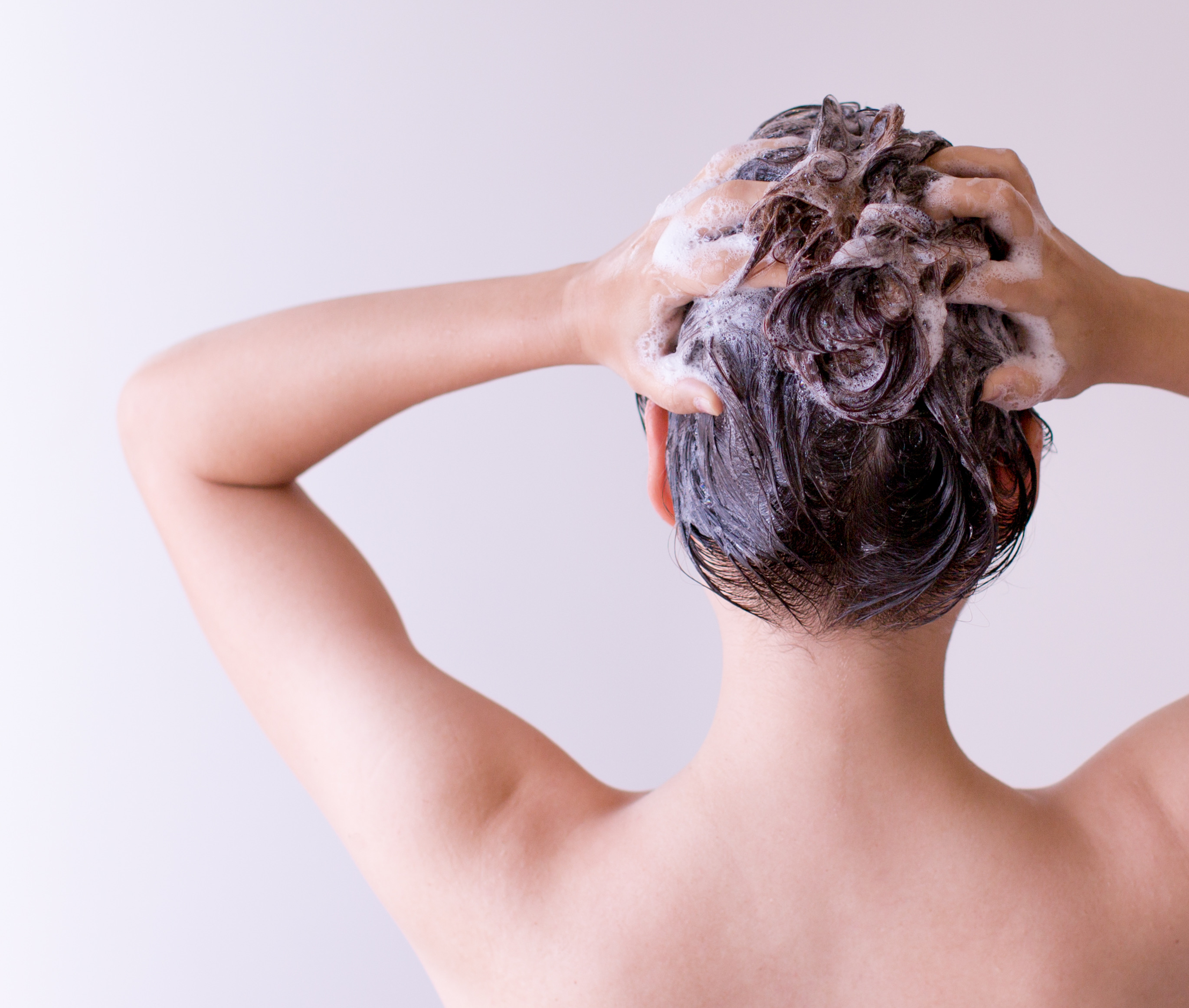 Young woman. Back shot. Hands on back of head. Hair has many suds from shampoo
