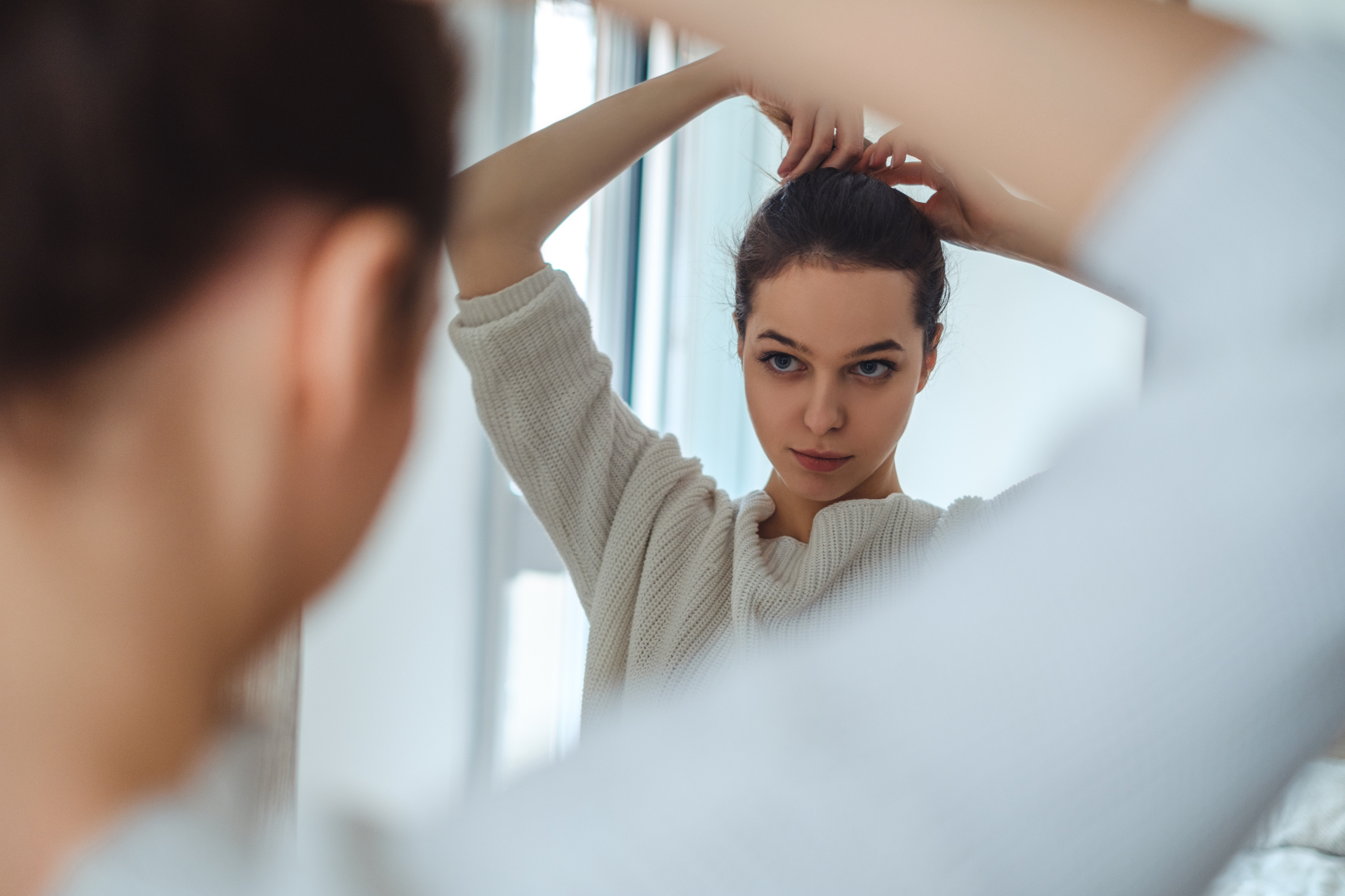 Beautiful girl looking in the mirror while making ponytail