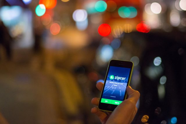 Hand holding a mobile showing the Zipcar app