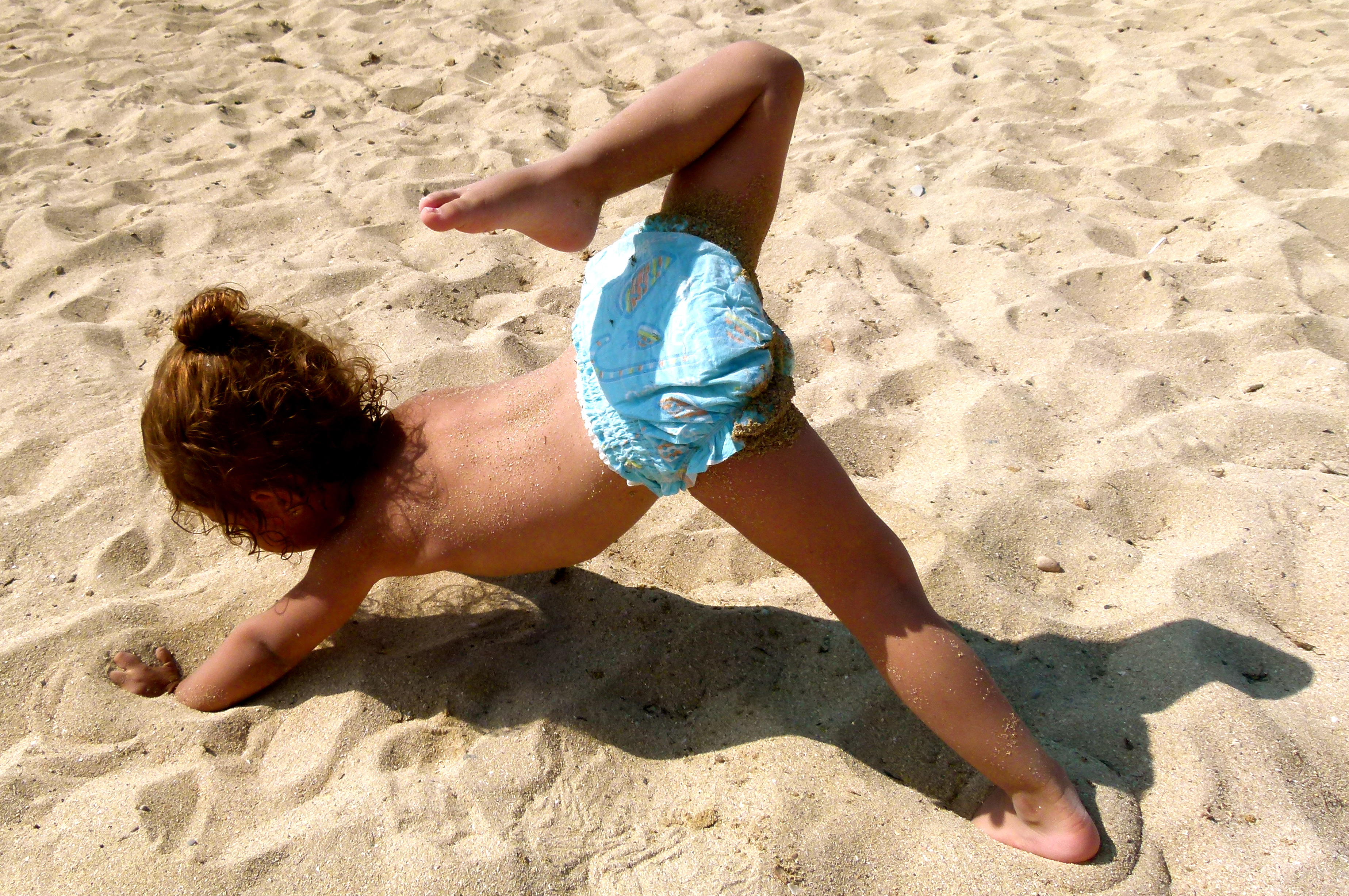 Toddler in nappy on the beach doing yoga