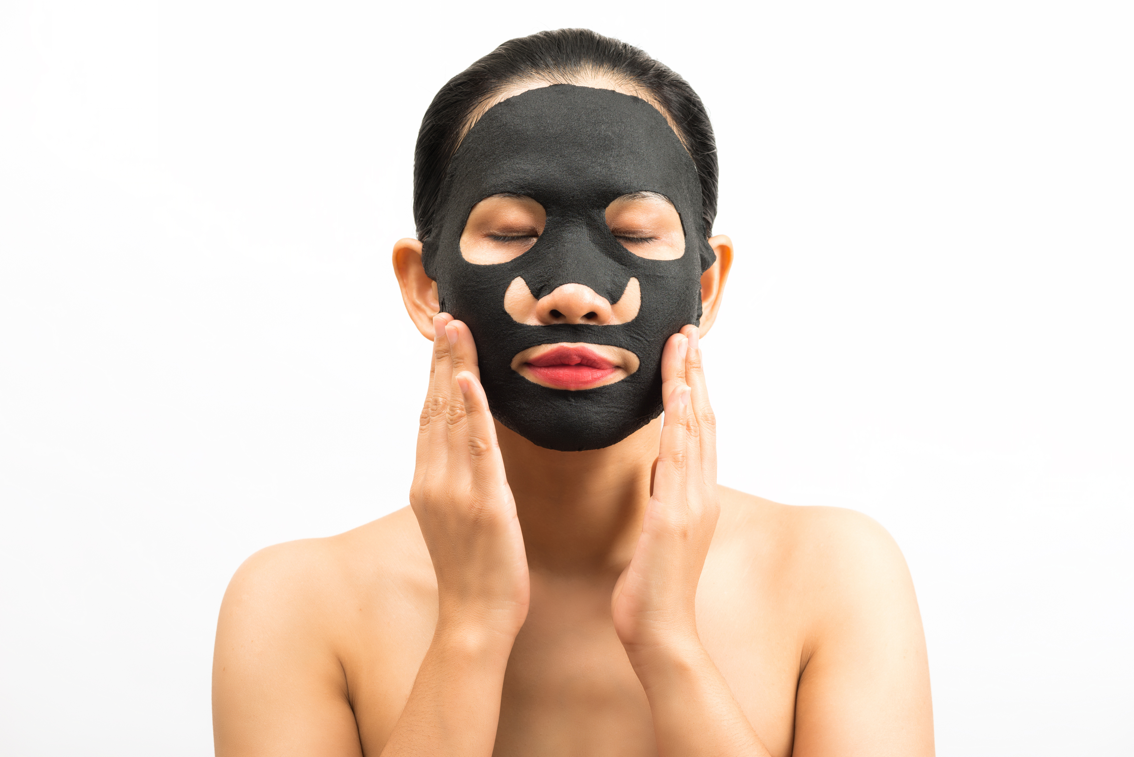 Young woman doing facial black mask sheet with purifying mask on her face