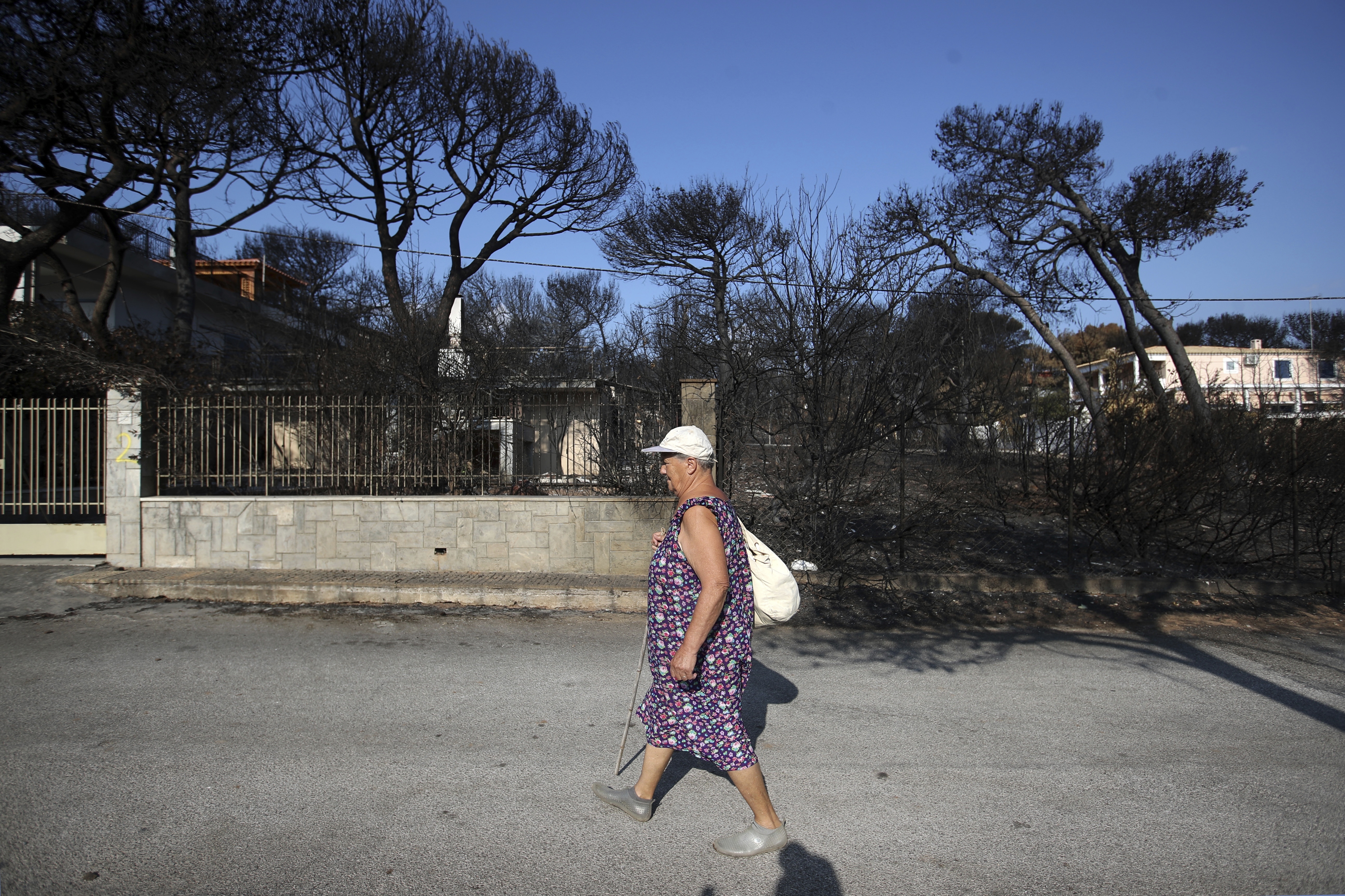 A woman walks in front of a burnt house in Mati , Greece