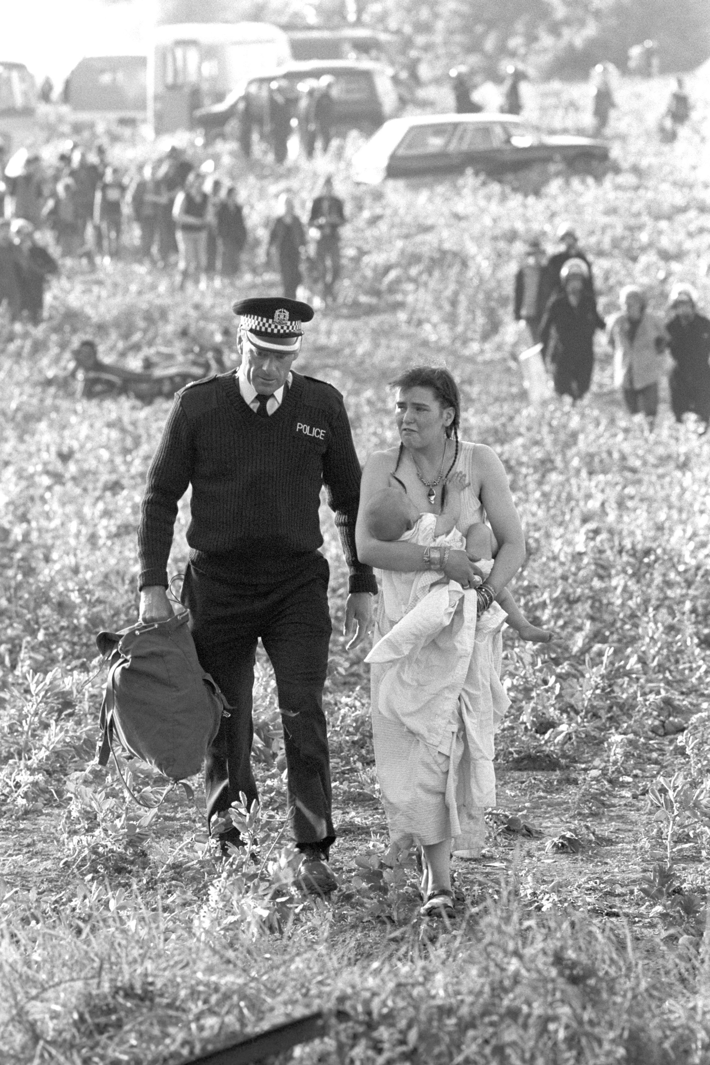 A woman holding a baby as she is led away by a policeman after violence erupted due to people attempting to hold a banned pop festival at Stonehenge in 1985