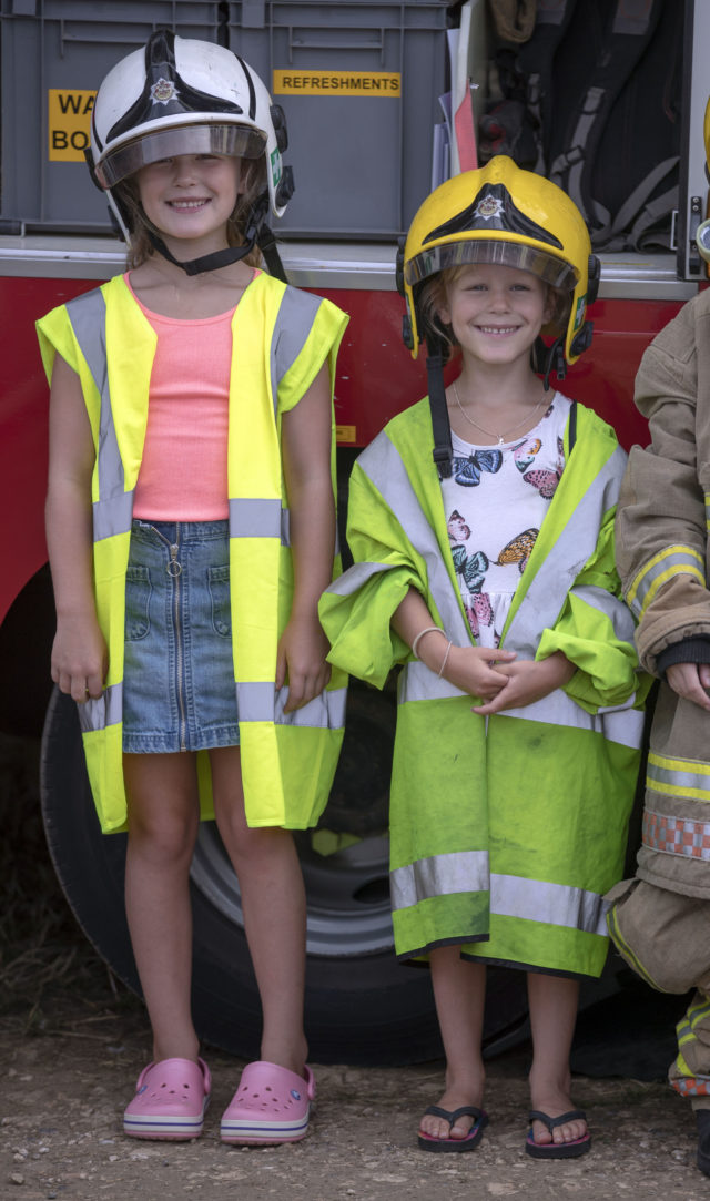 Savannah and Isla trying on firefighters clothing at the Festival of British Eventing at Gatcombe Park, Gloucestershire