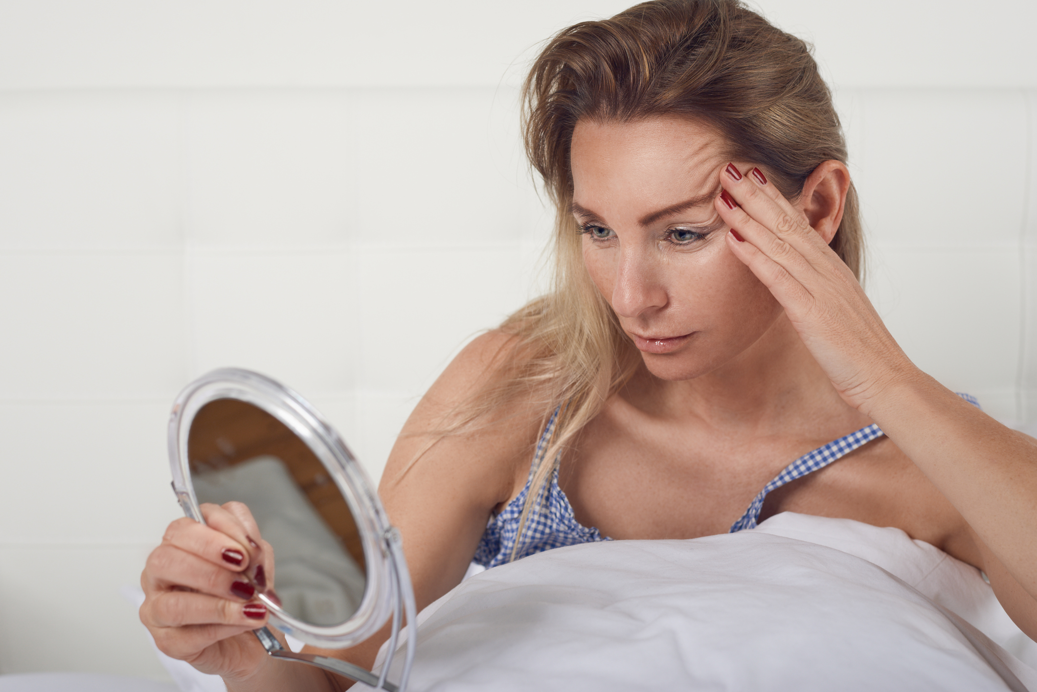 Portrait of a worried woman thinking of aging while looking in the mirror at her face and her facial wrinkles