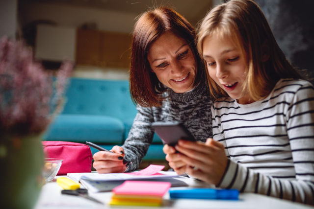 Mother and daughter doing homework late at night and using smart phone
