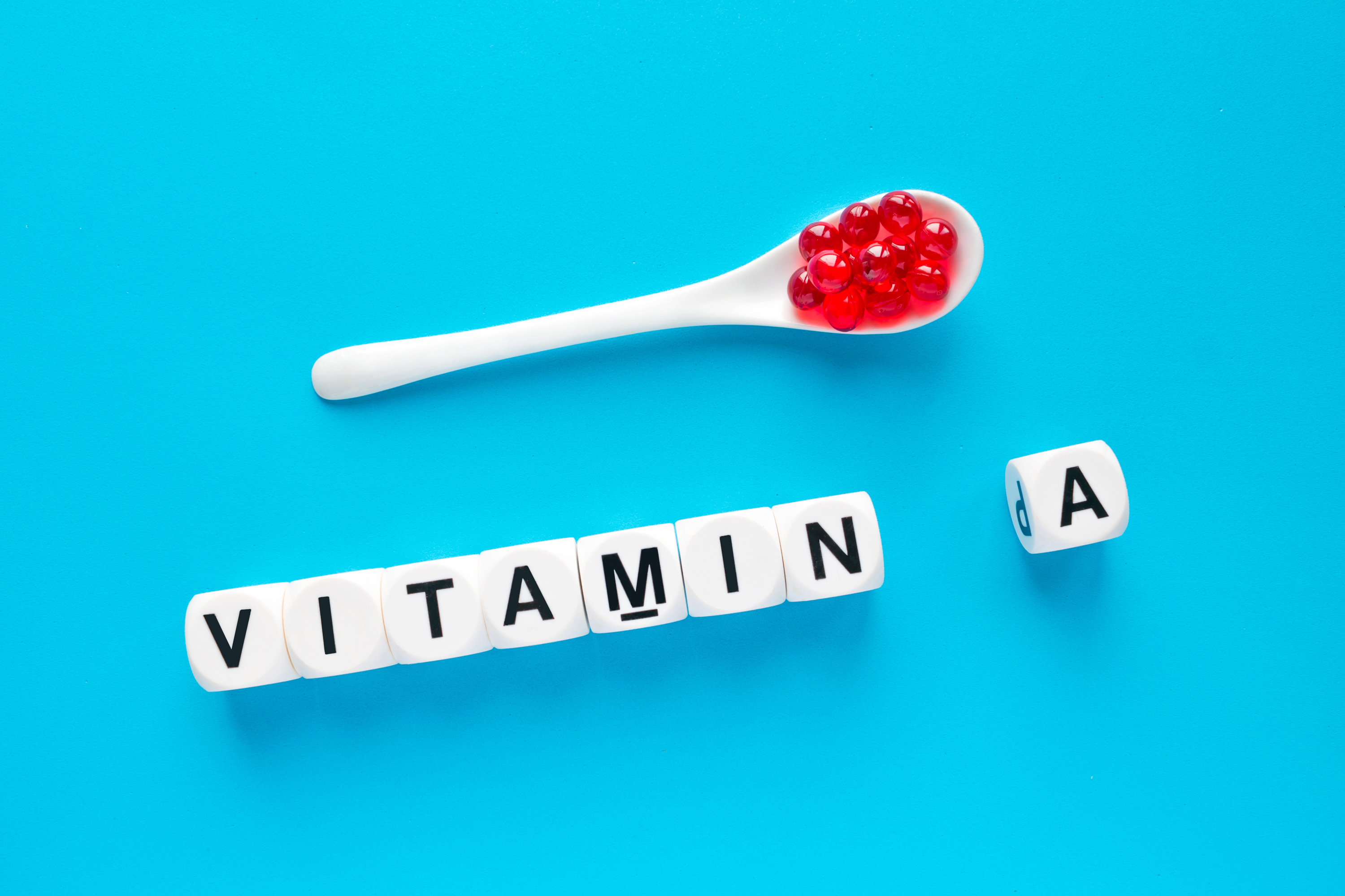 Red capsules in the white spoon and the word vitamin A from white cubes with letters on a blue background. healthy and medical concept. retinol, retinal, retinoic acid, provitamin A, carotenoid, beta-carotene health benefits