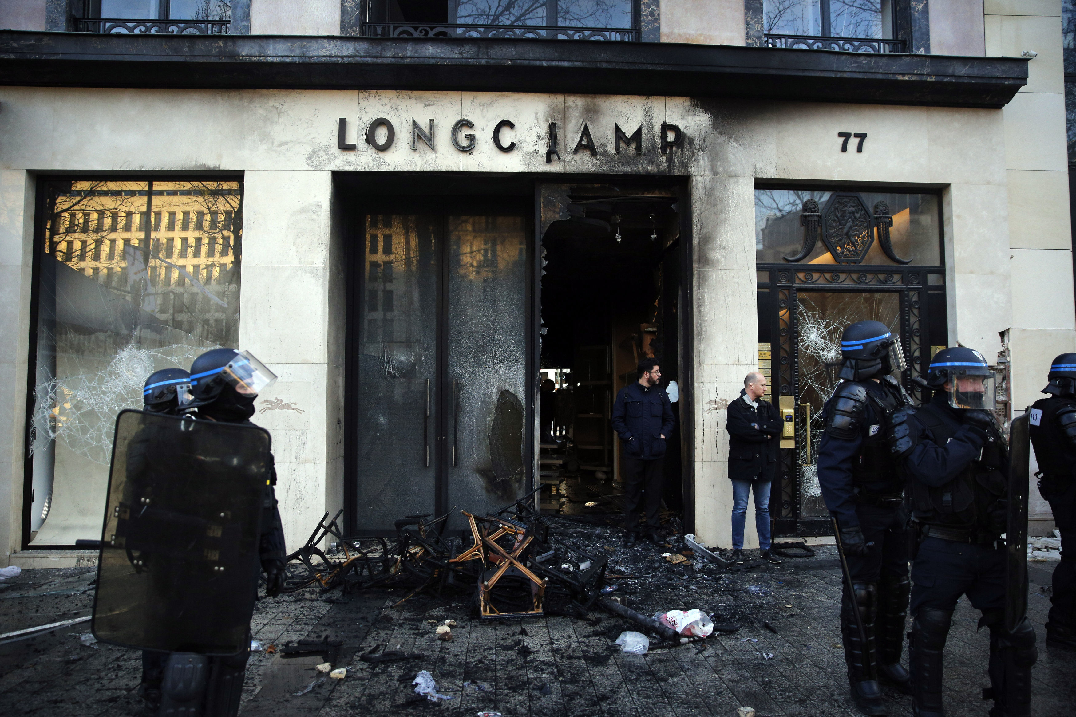 Riot police stand in front of a burned store 