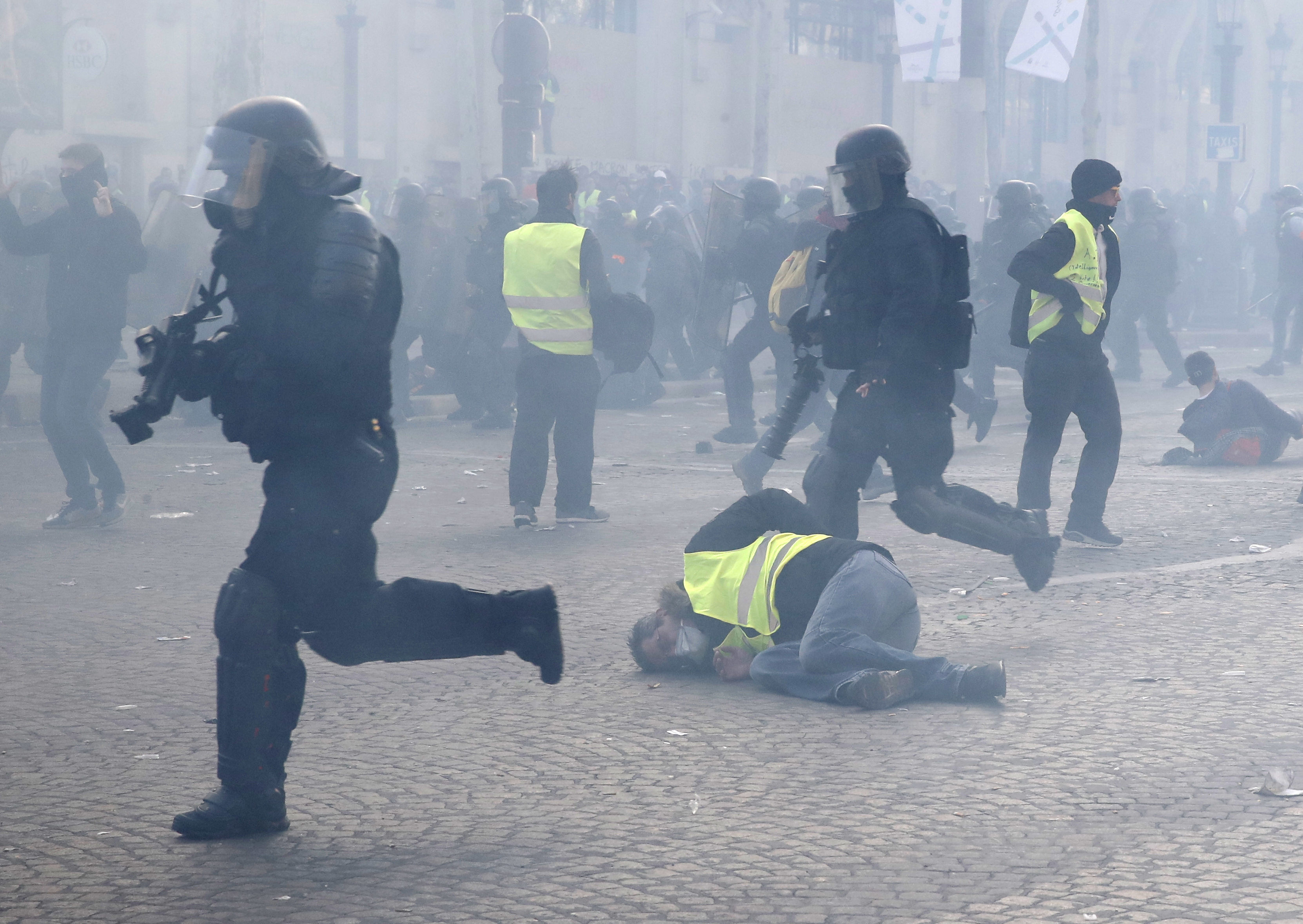 Riot police officers charge as a yellow vest demonstrators fall in Paris