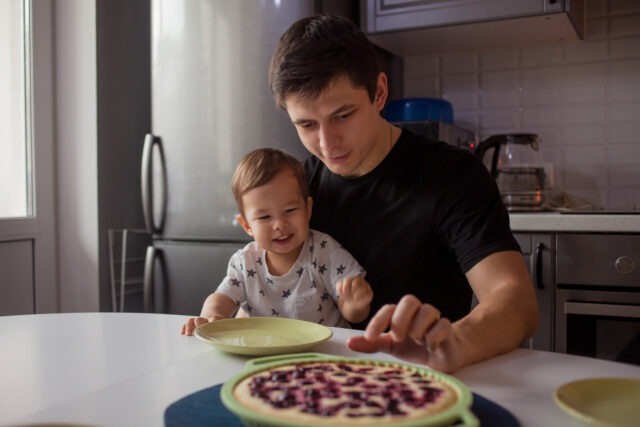 Father and son in the kitchen. kid wants a delicious hot cake. Young man with son, happy family