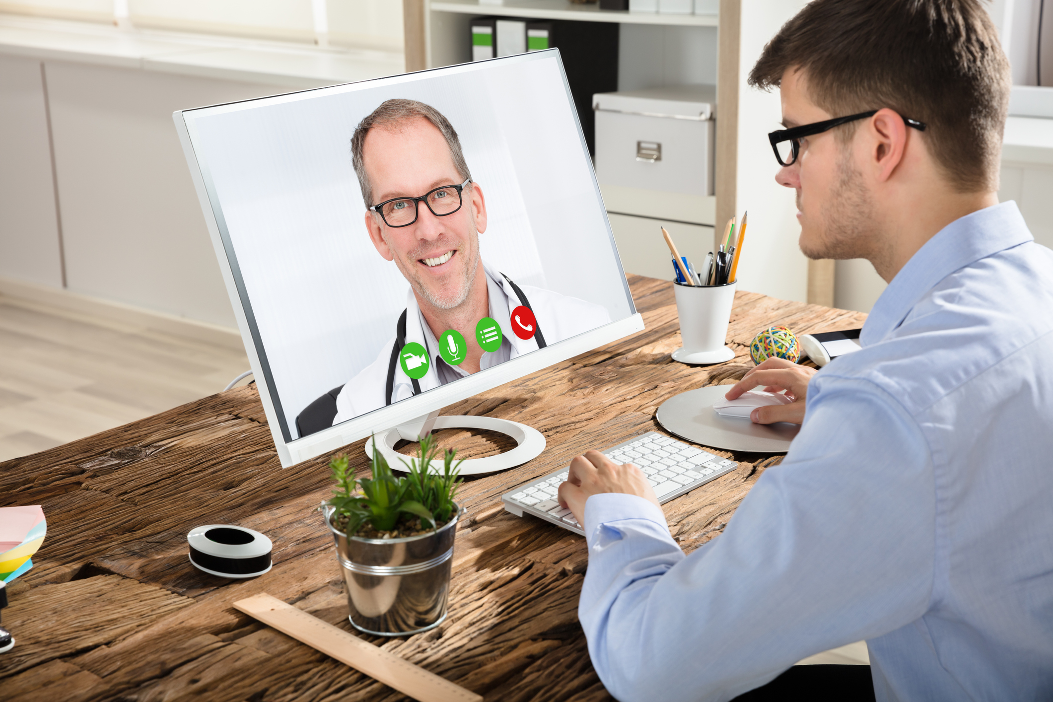 Young Businessman Video Conferencing With Smiling Male Doctor On Computer In Office