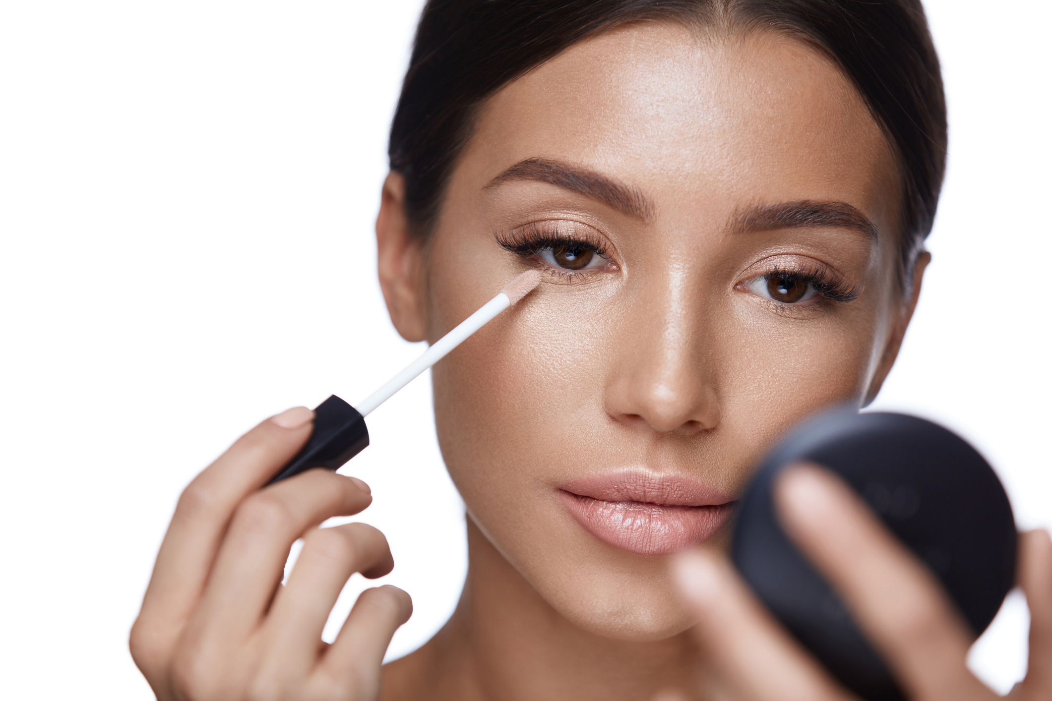 Beauty Face. Closeup Of Sexy Young Woman With Concealer Brush And Mirror In Hands. Portrait Of Beautiful Healthy Female Model Applying Concealer Under Eyes
