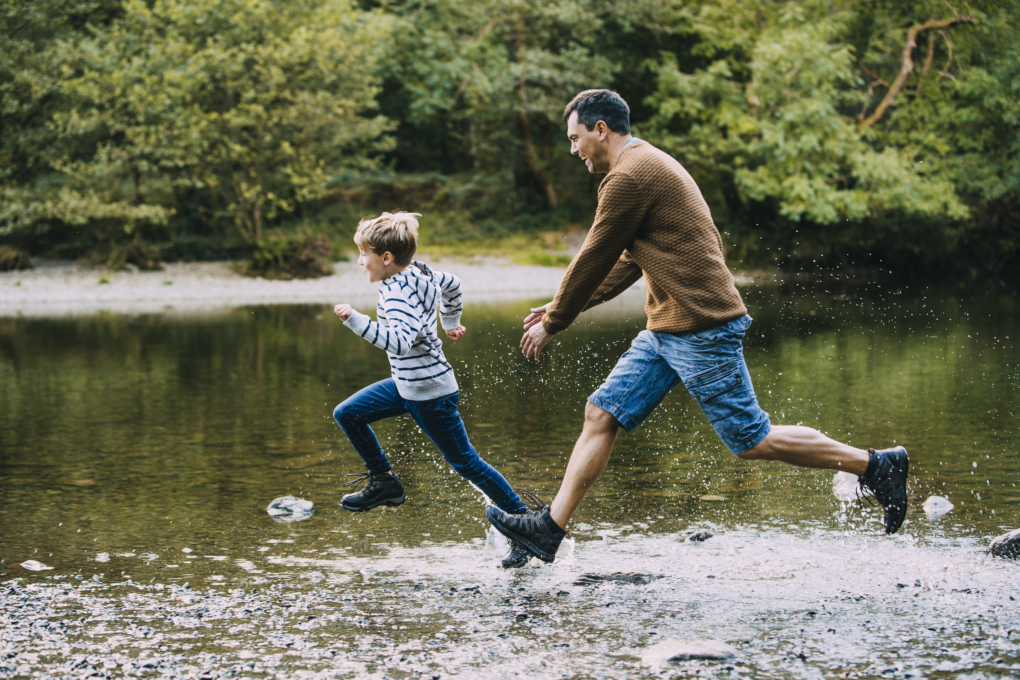Little boy is being chased in to the lake by his father while they are out hiking.