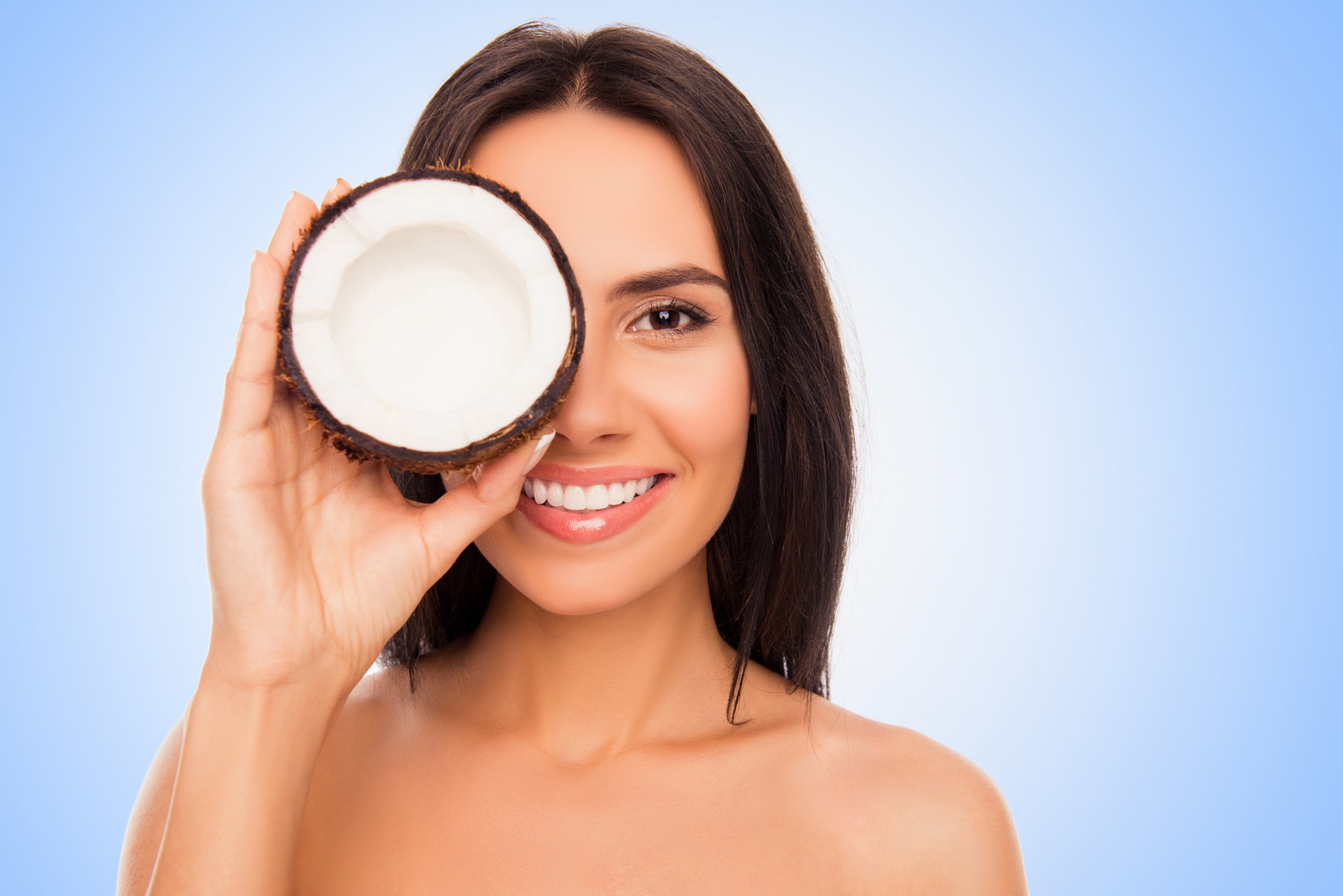 Cheerful pretty young woman holdind coconut near her eyes