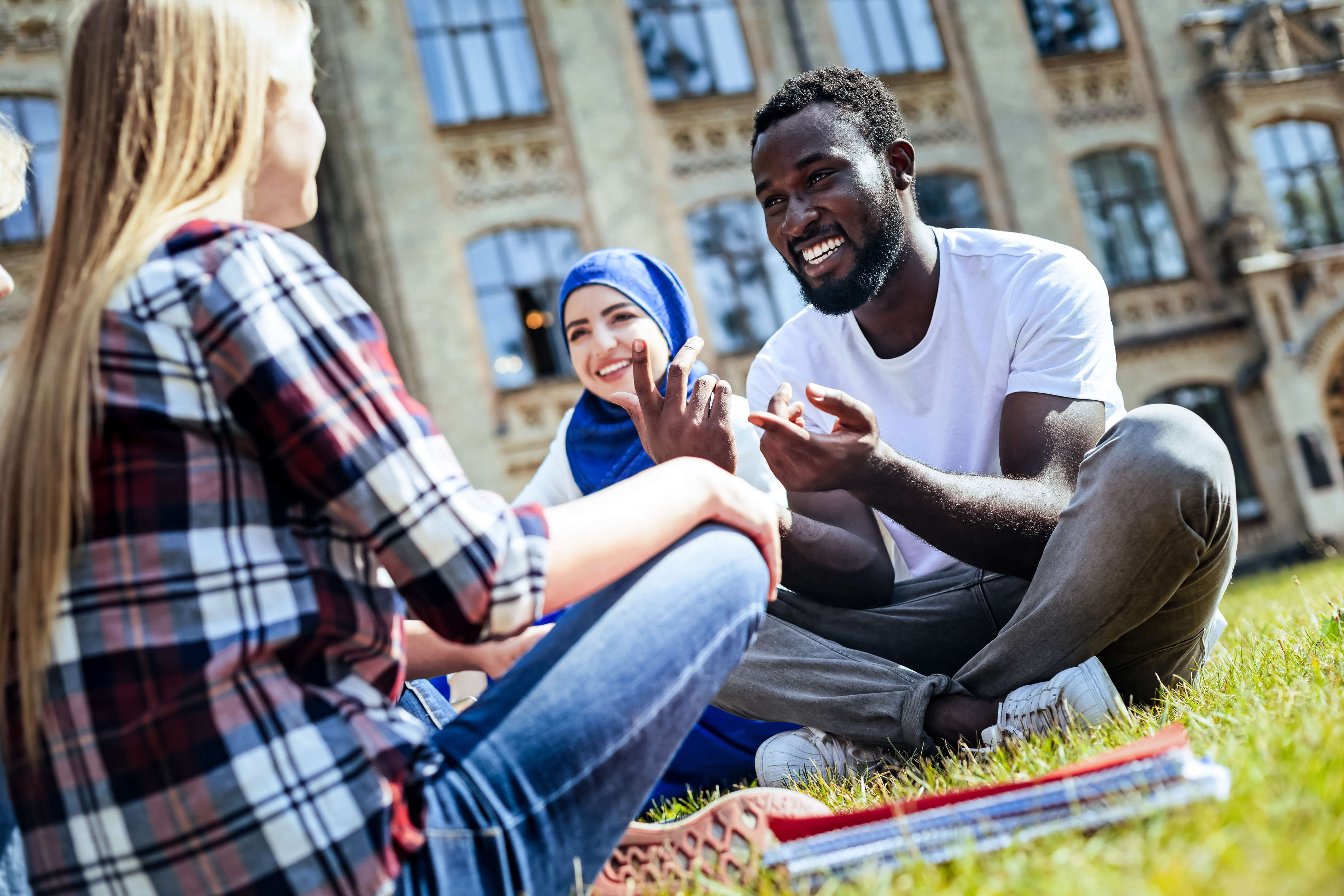 Pleasant conversation. Low angle shot of young people grinning broadly while sitting on grass and chatting together outdoors.