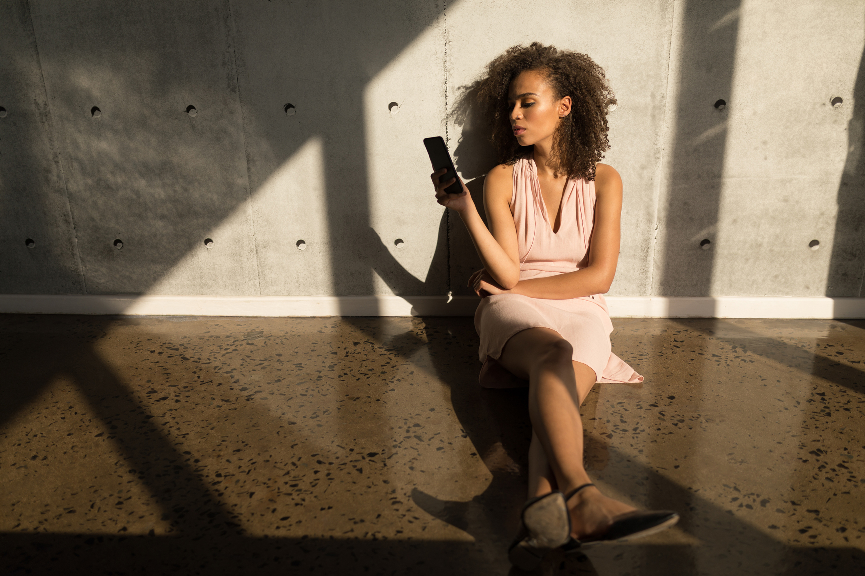 Front view of pretty mixed-race female executive using mobile phone while sitting on the ground in modern office