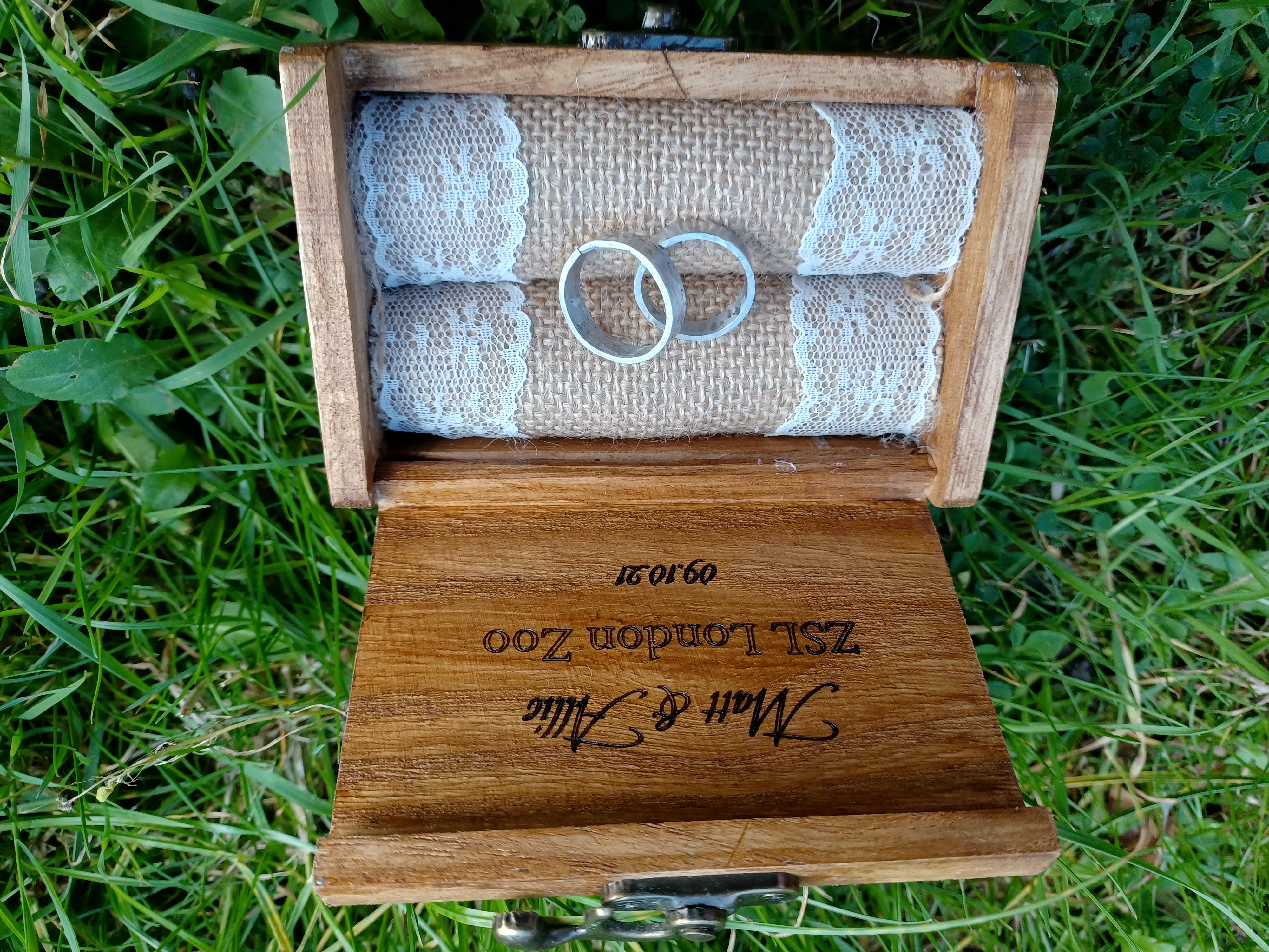 Two silver rings sit within a light brown wooden box on a green background