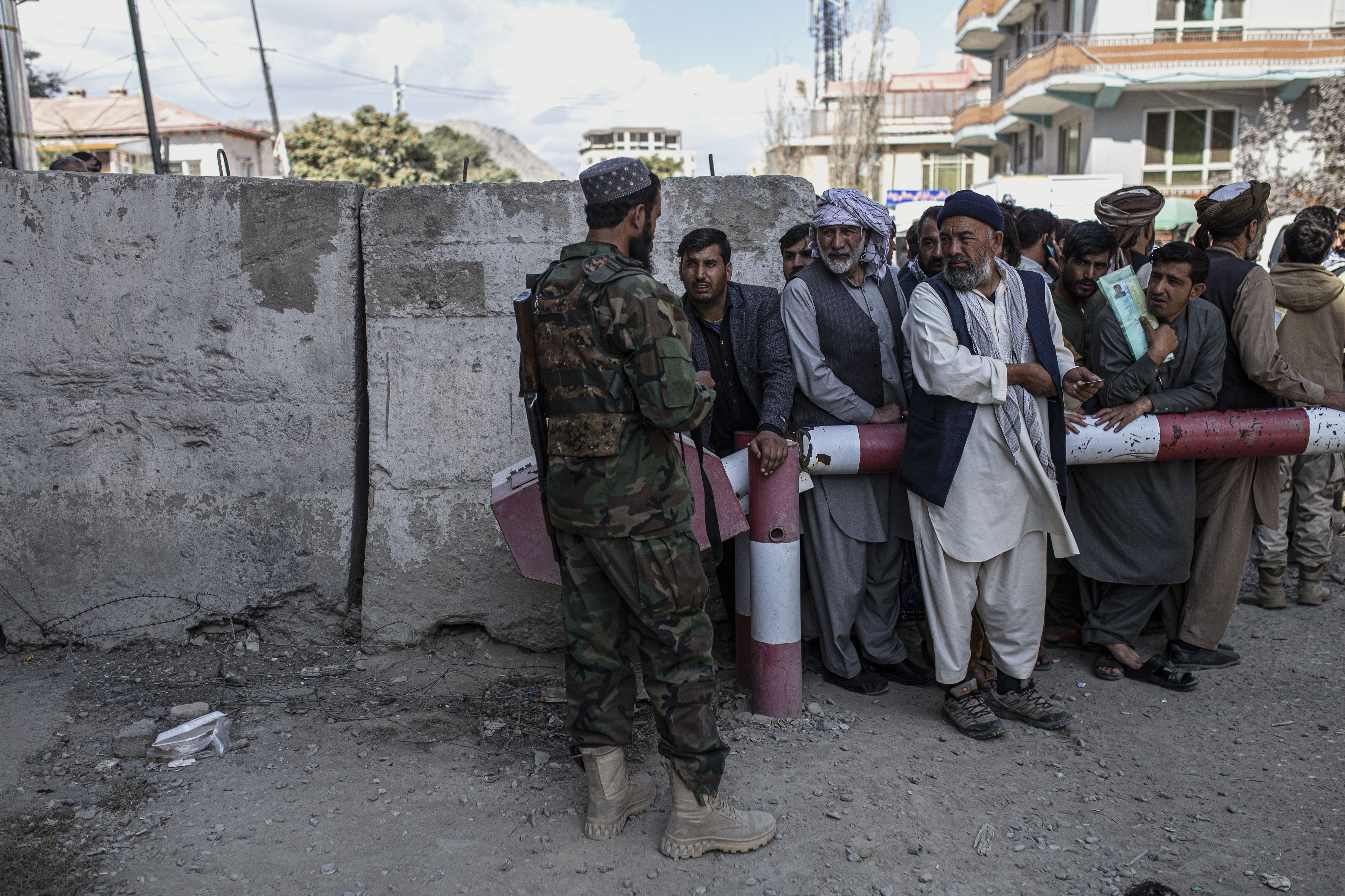 People gather outside as a Taliban fighter controls the entrance to the government passport office