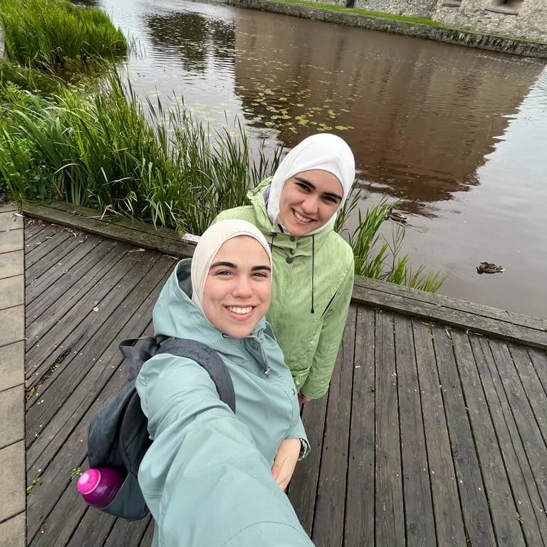 A photo of Laila Saliekh with her sister Katrena Saleh standing on a bridge in front of some water smiling at the camera