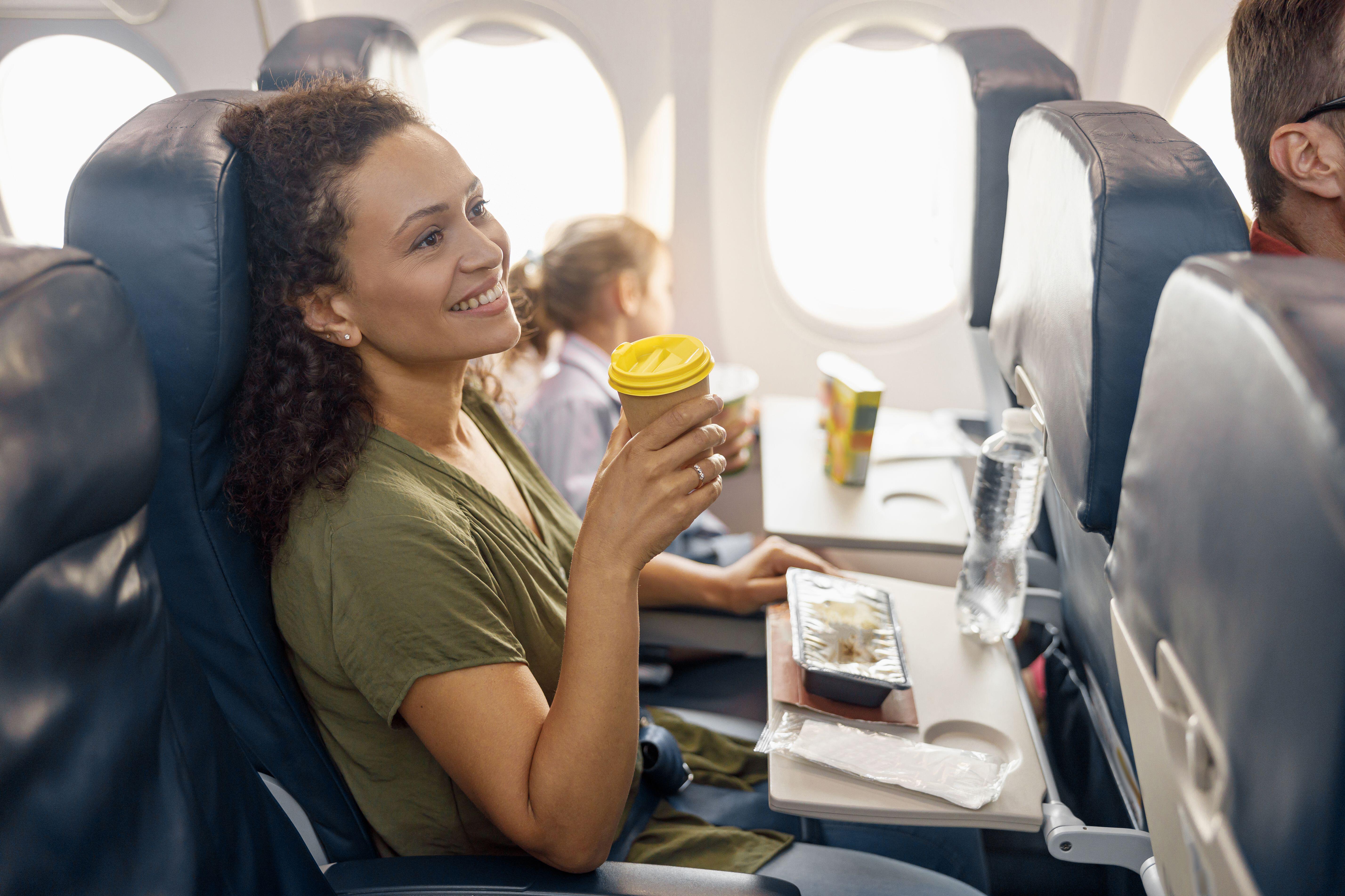 Happy female passenger drinking coffee and smiling while female flight attendant serving lunch on board