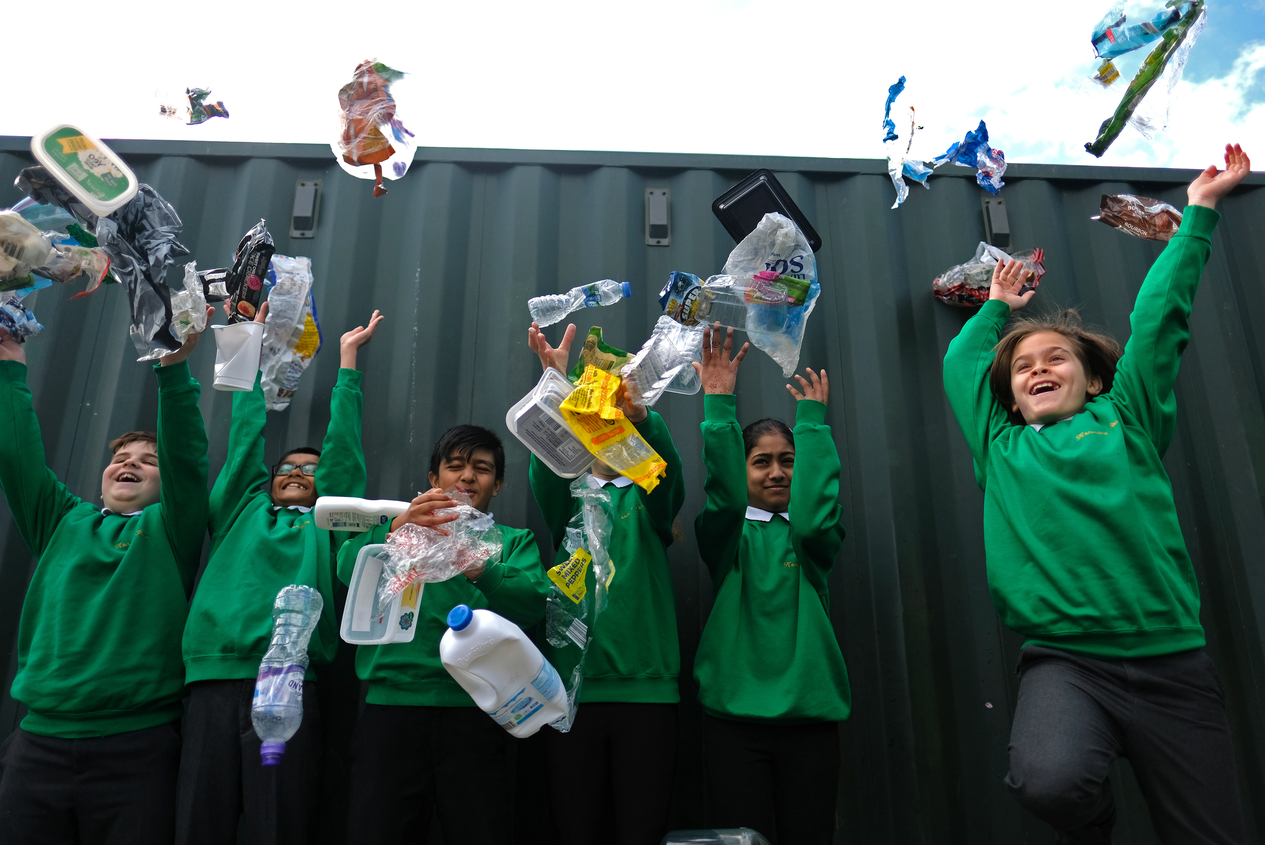 A line of children in green school jumpers throw plastic items into the air