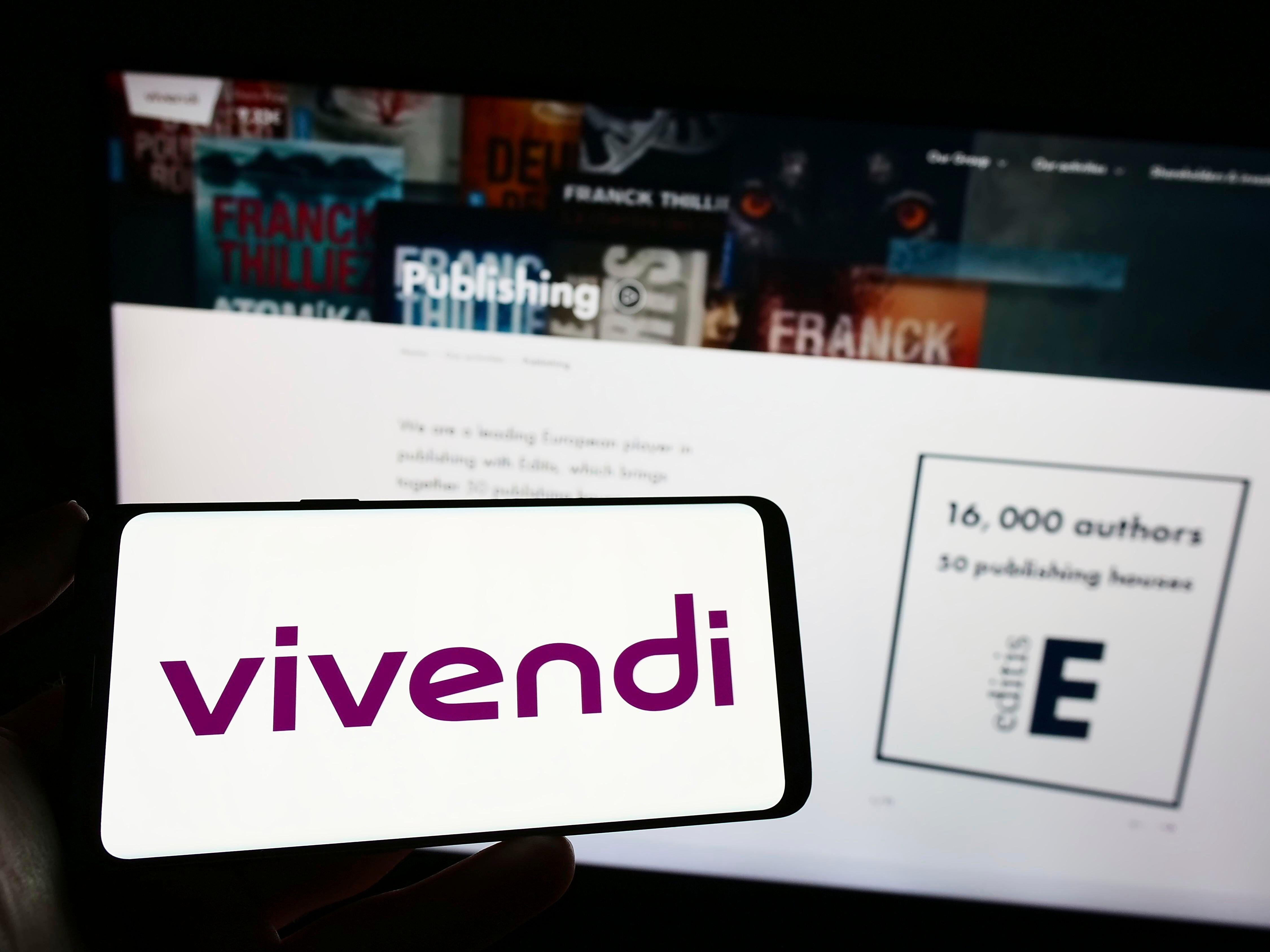 A person holding a phone with a logo of Vivendi on the screen in front of a business webpage for the company