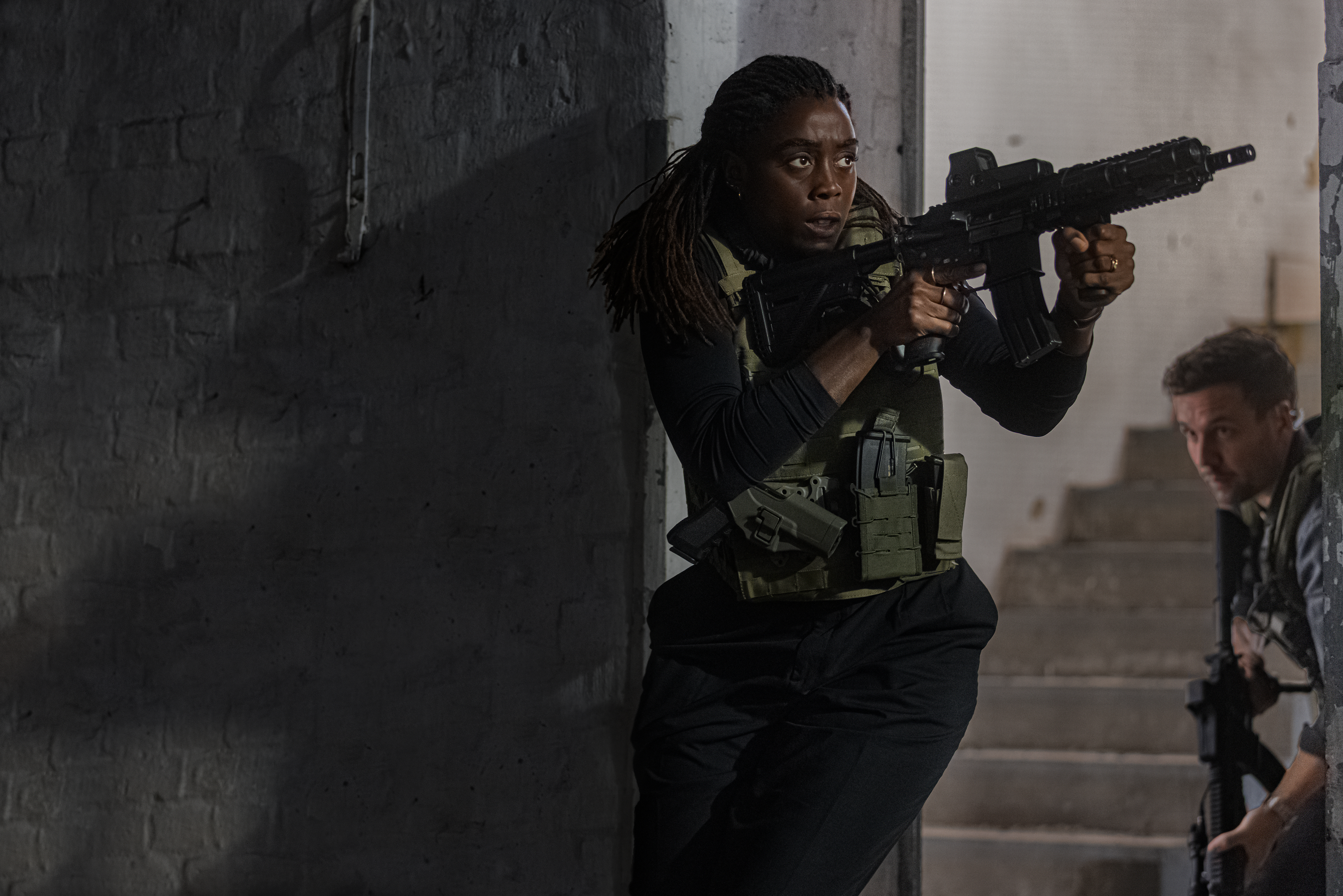 Lashana Lynch in character, with military vest and gun