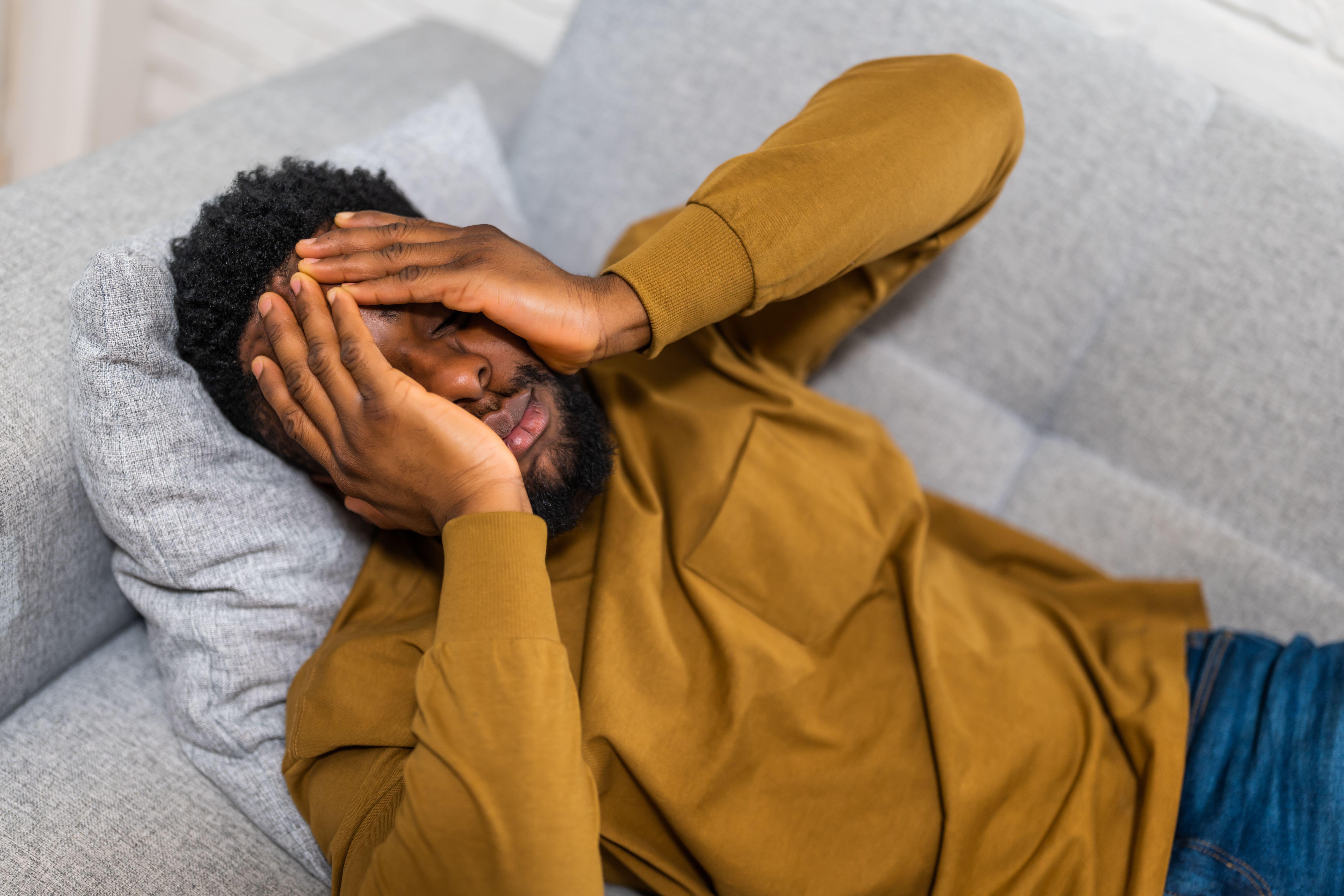 Exhausted man lying on his sofa with his hands covering his face