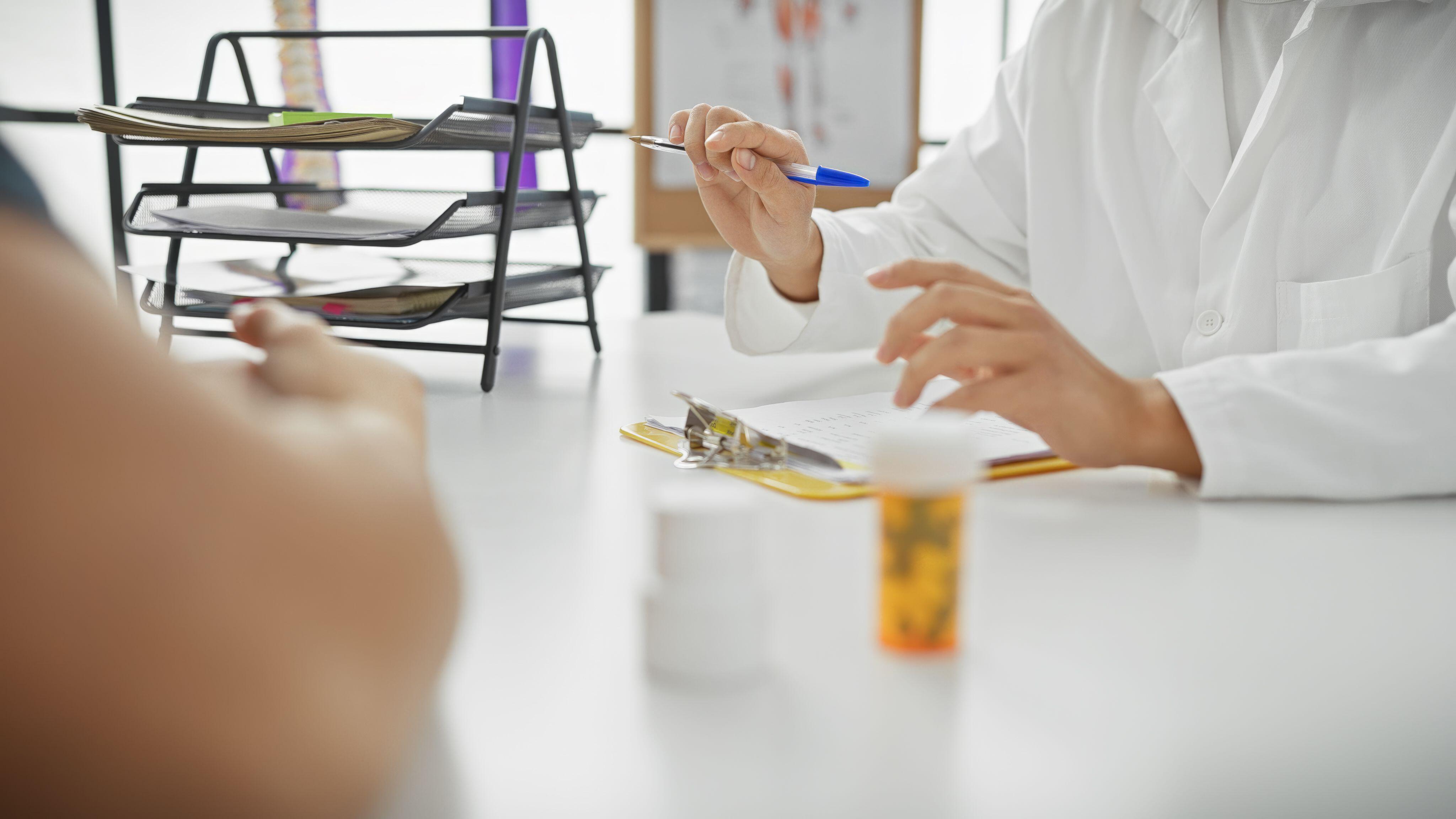 Doctor prescribing medication to a male patient in a bright, modern clinic, captured over the shoulder with focus on the consultation.