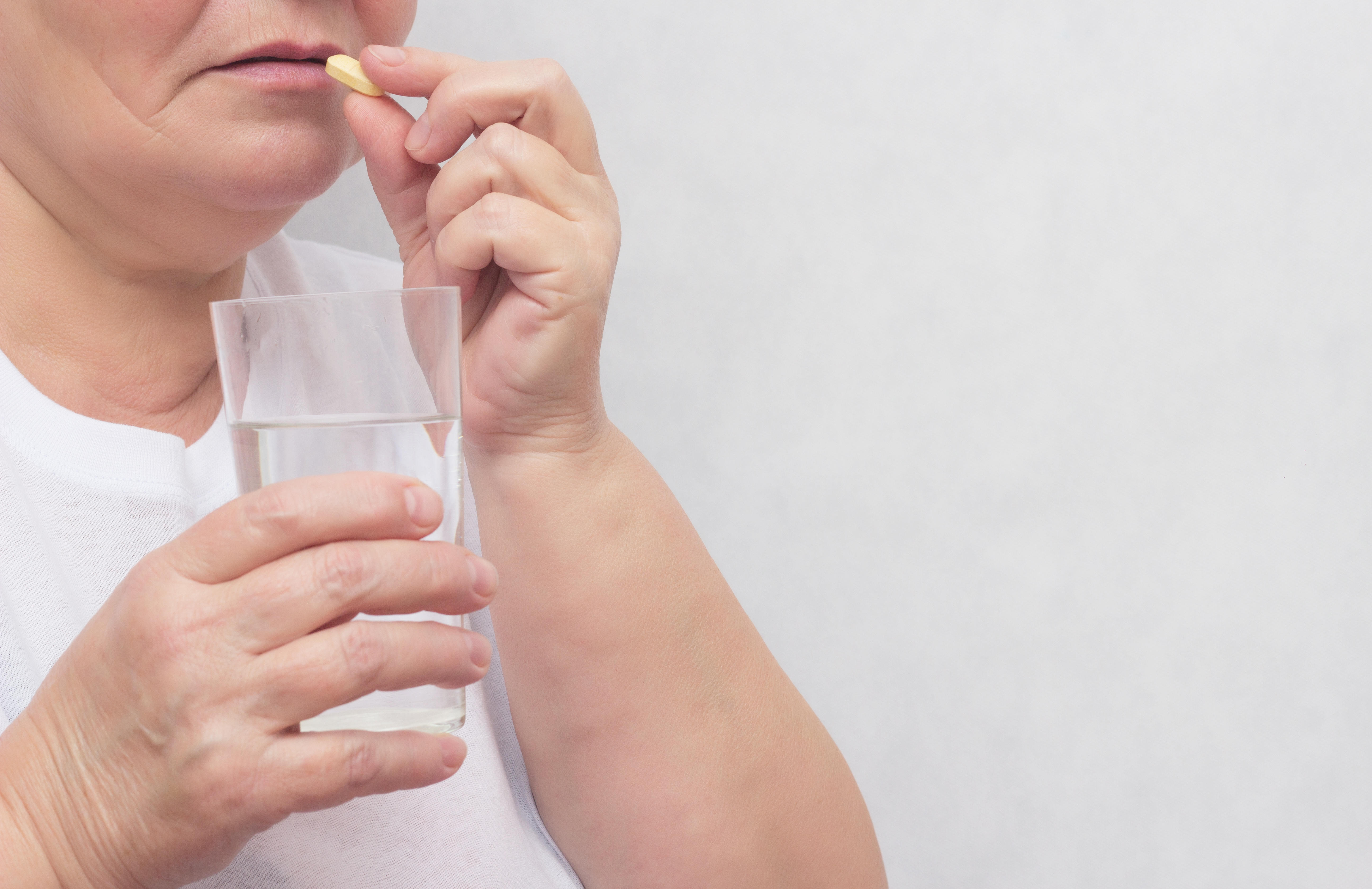 Woman holding a glass of water and taking a tablet