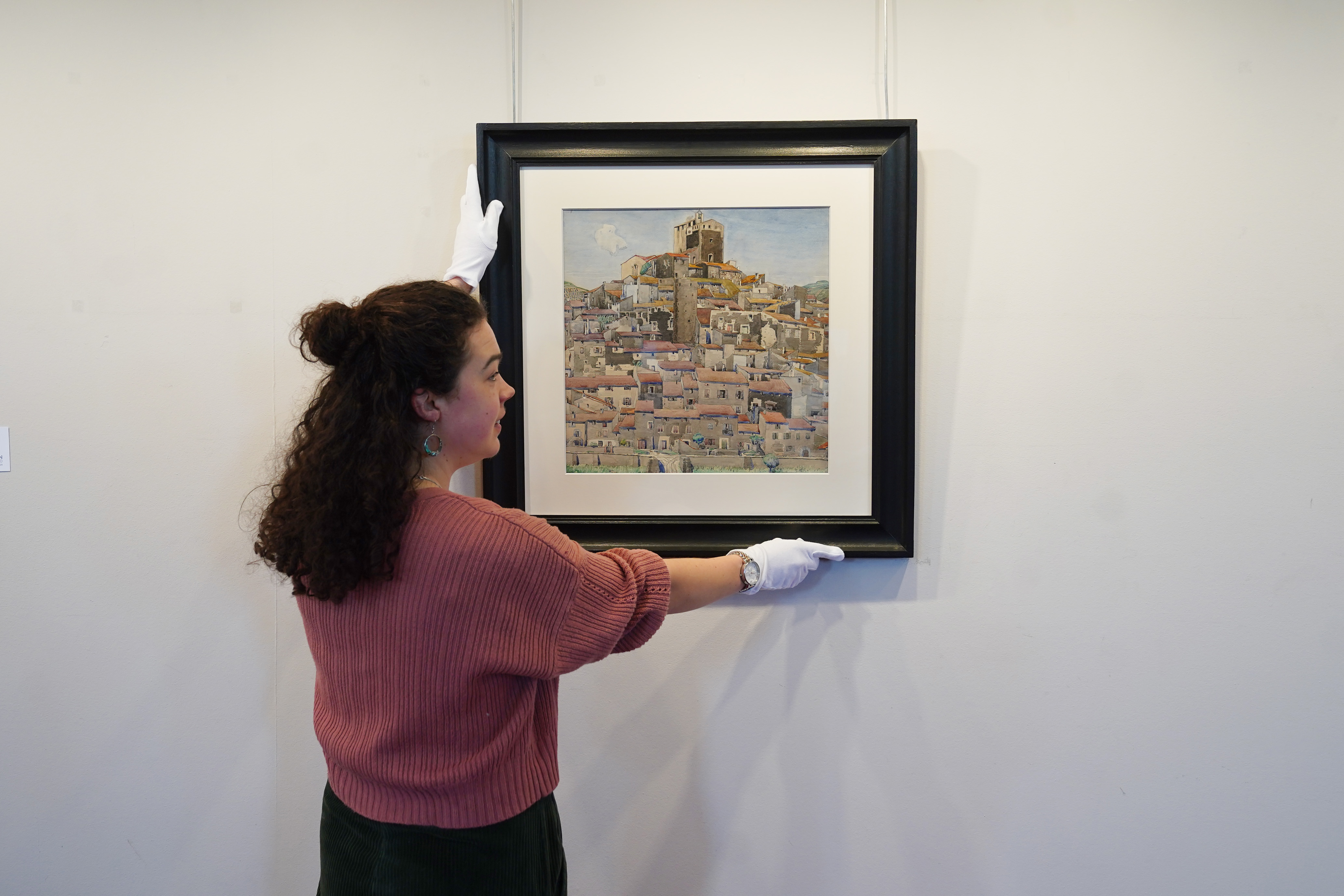 Charles Rennie Mackintosh's watercolour Bouleternere, in a black frame, is placed on a wall by a woman