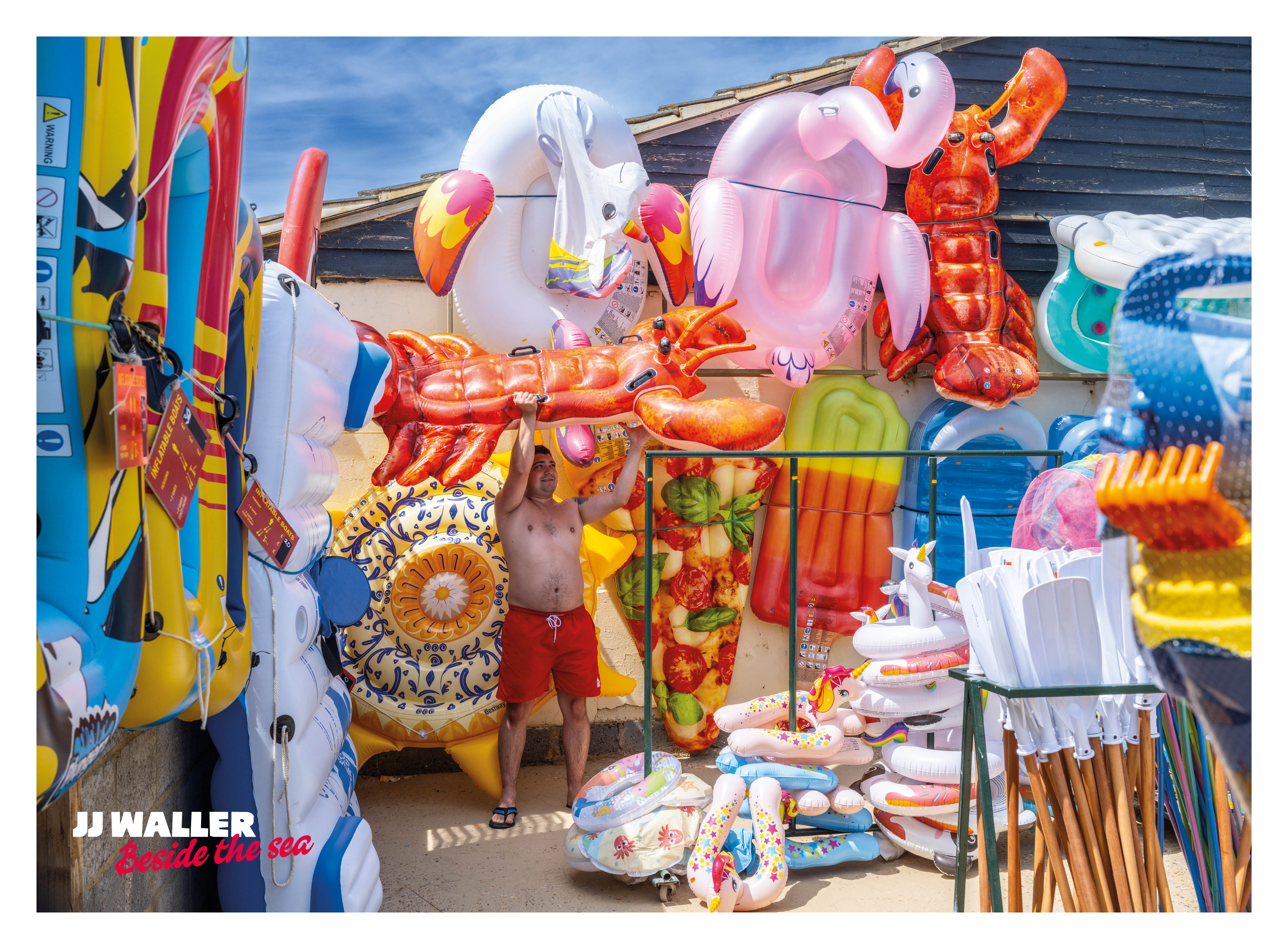 A man holds a lobster inflatable beside a beach hut