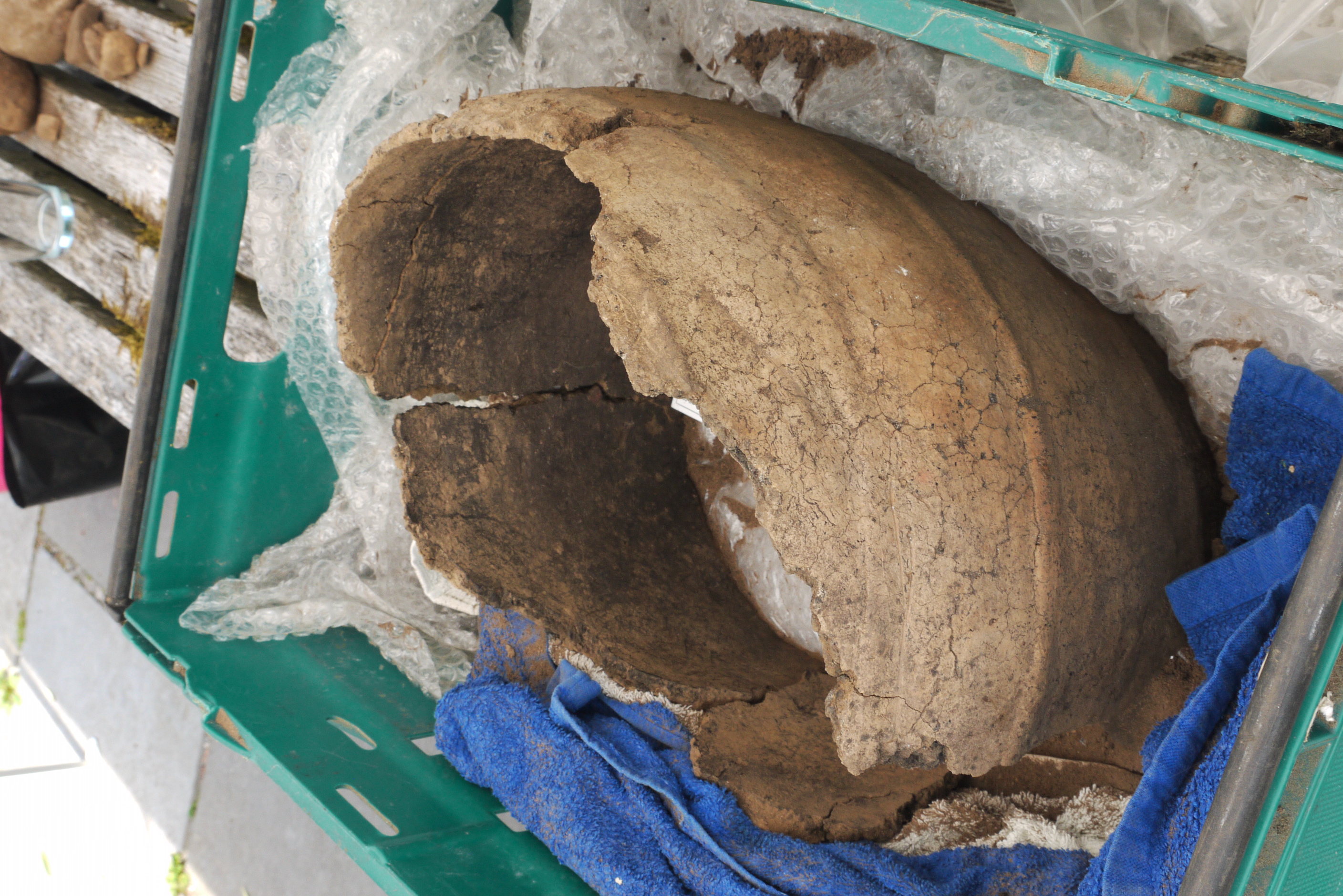 An ancient looking, partially broken urn sitting in a crate