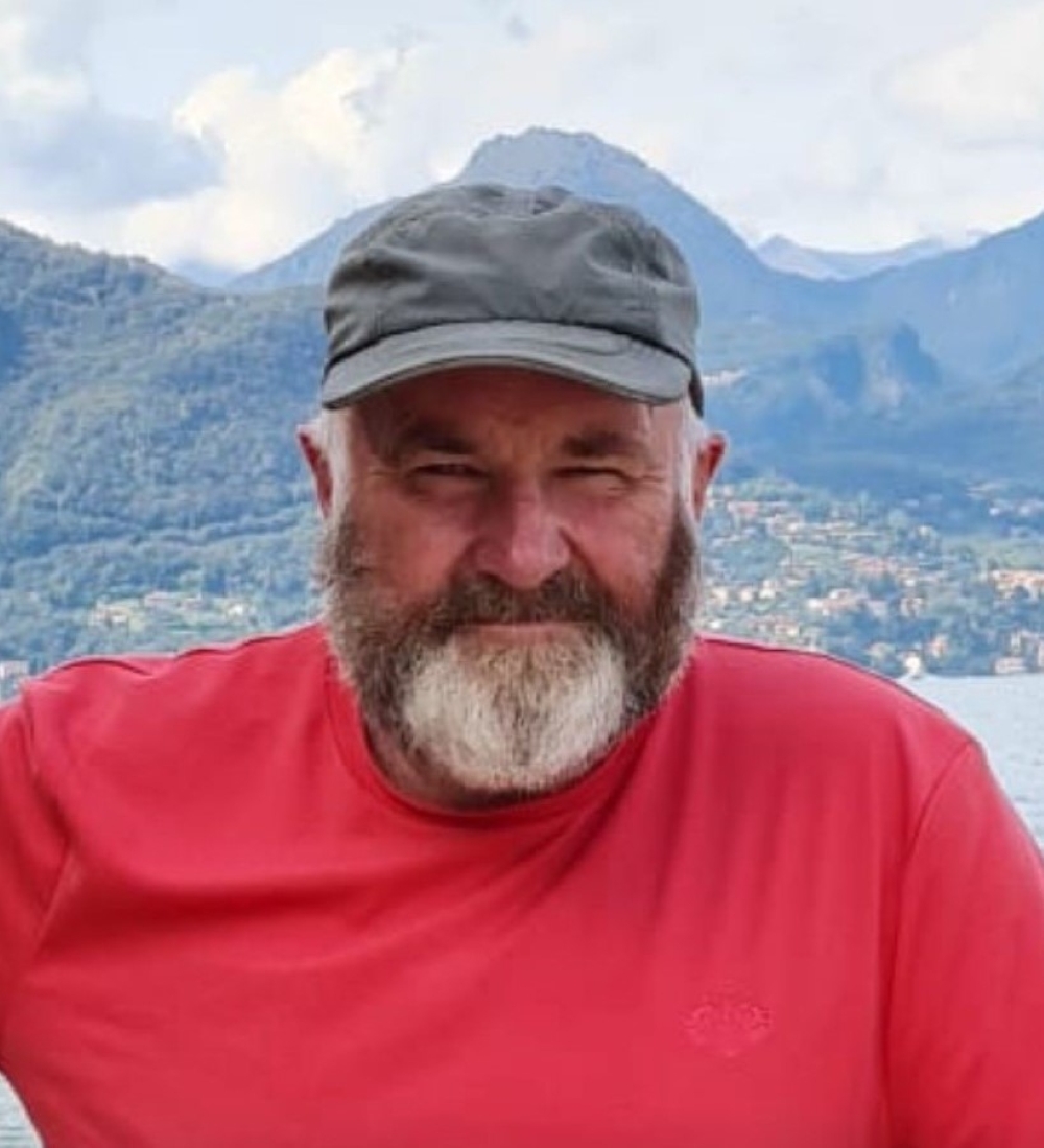 A smiling man with a full beard, cap and red t-shirt