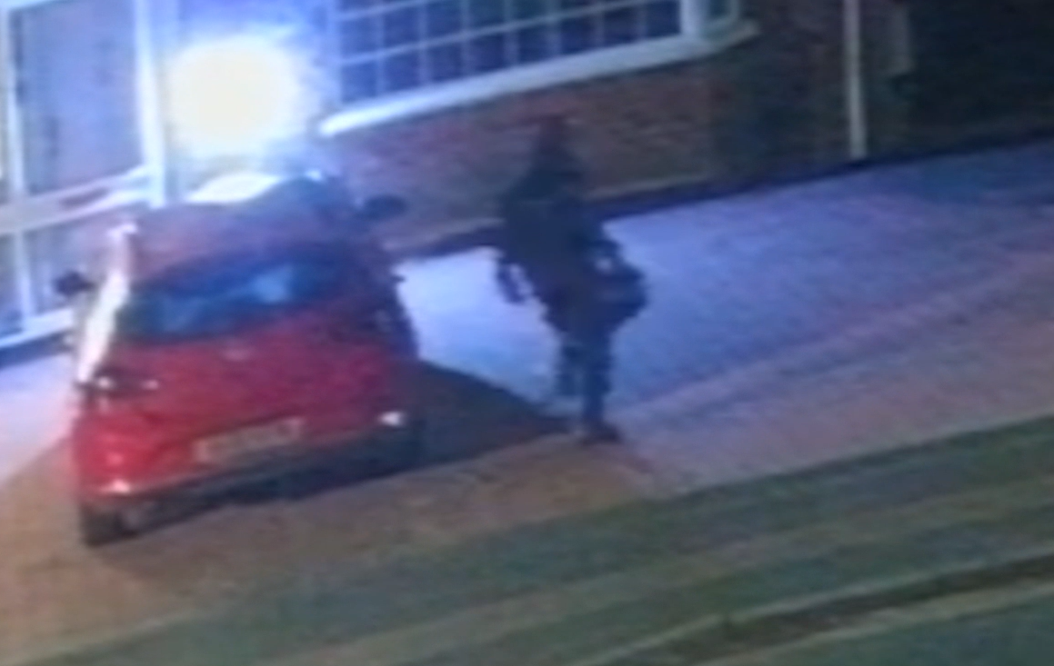 CCTV image of a figure carrying a contained towards a house