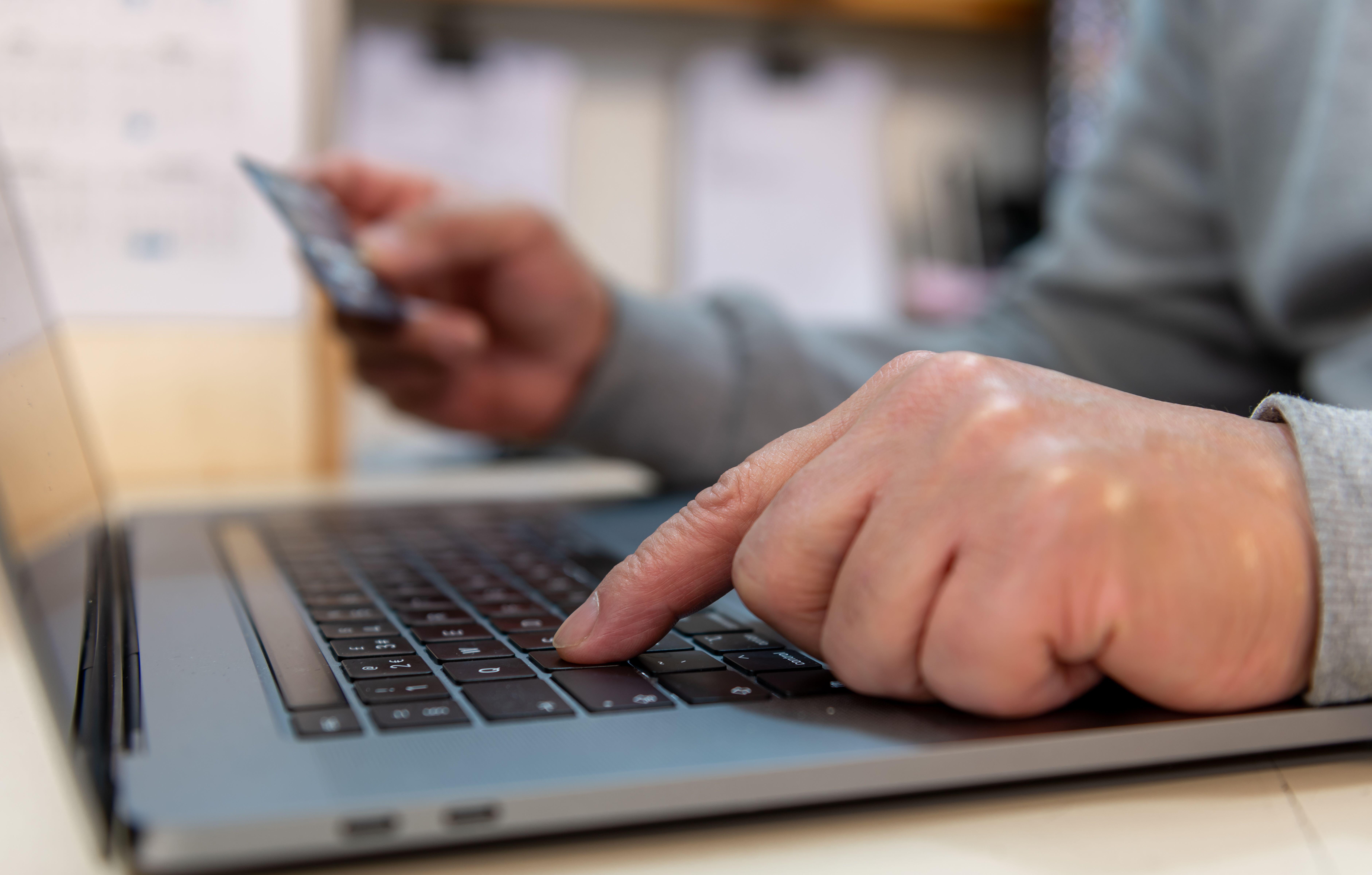 A man holding a bank card while using a laptop