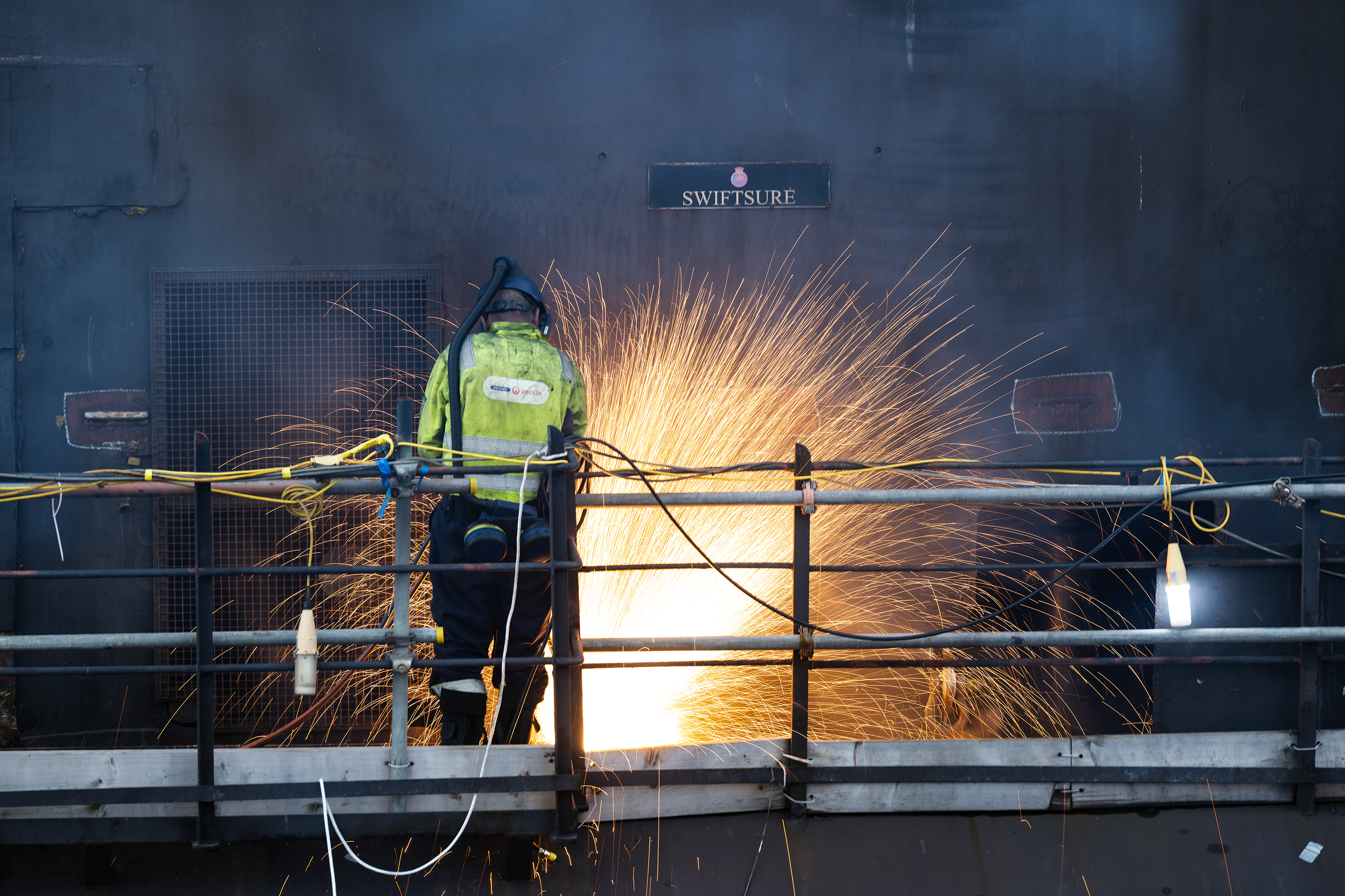 Sparks flying as a man in protective gear works on a submarine