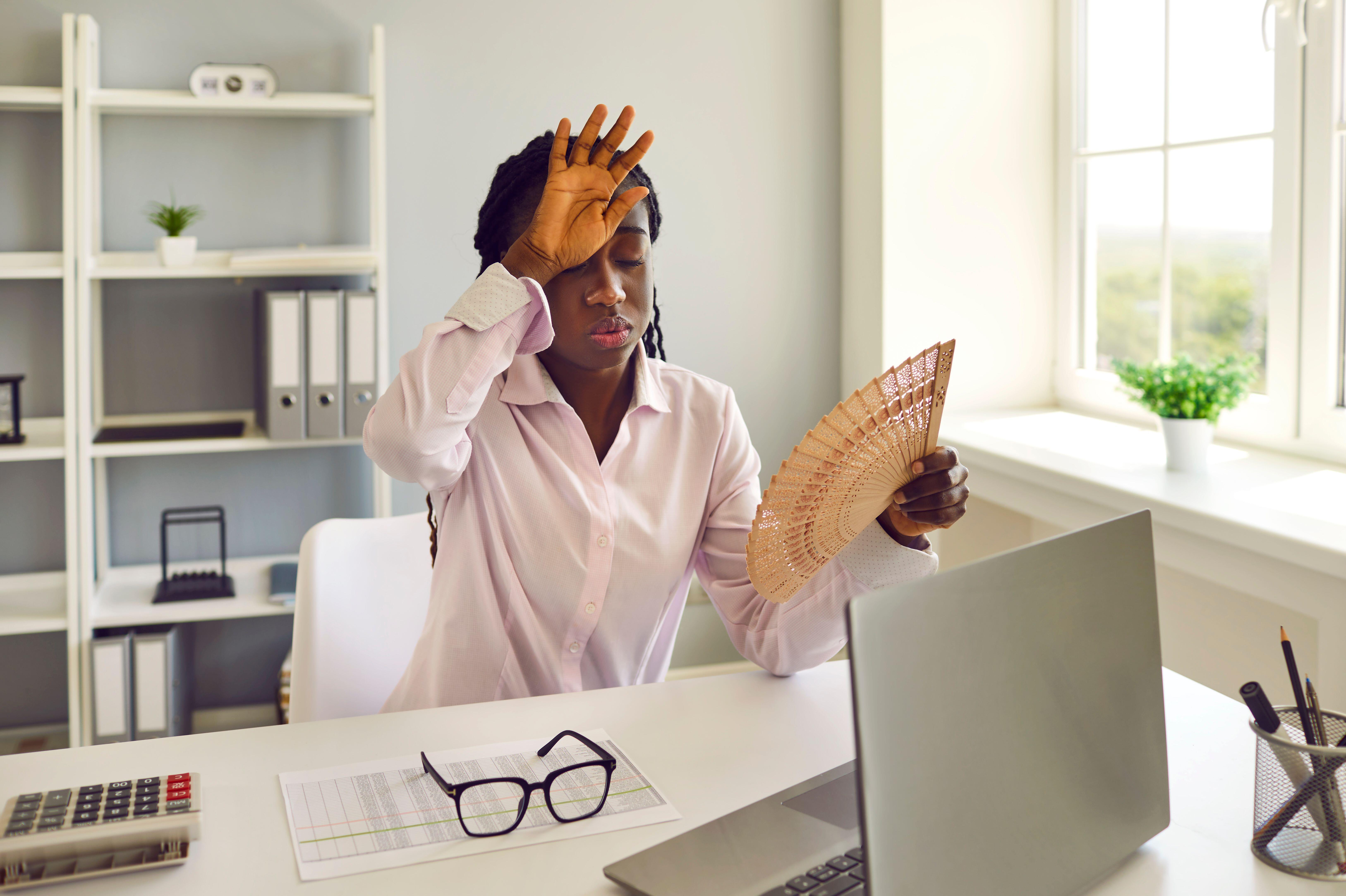 Exhausted woman at her workplace in office suffering from hot weather and lack of air conditioning.