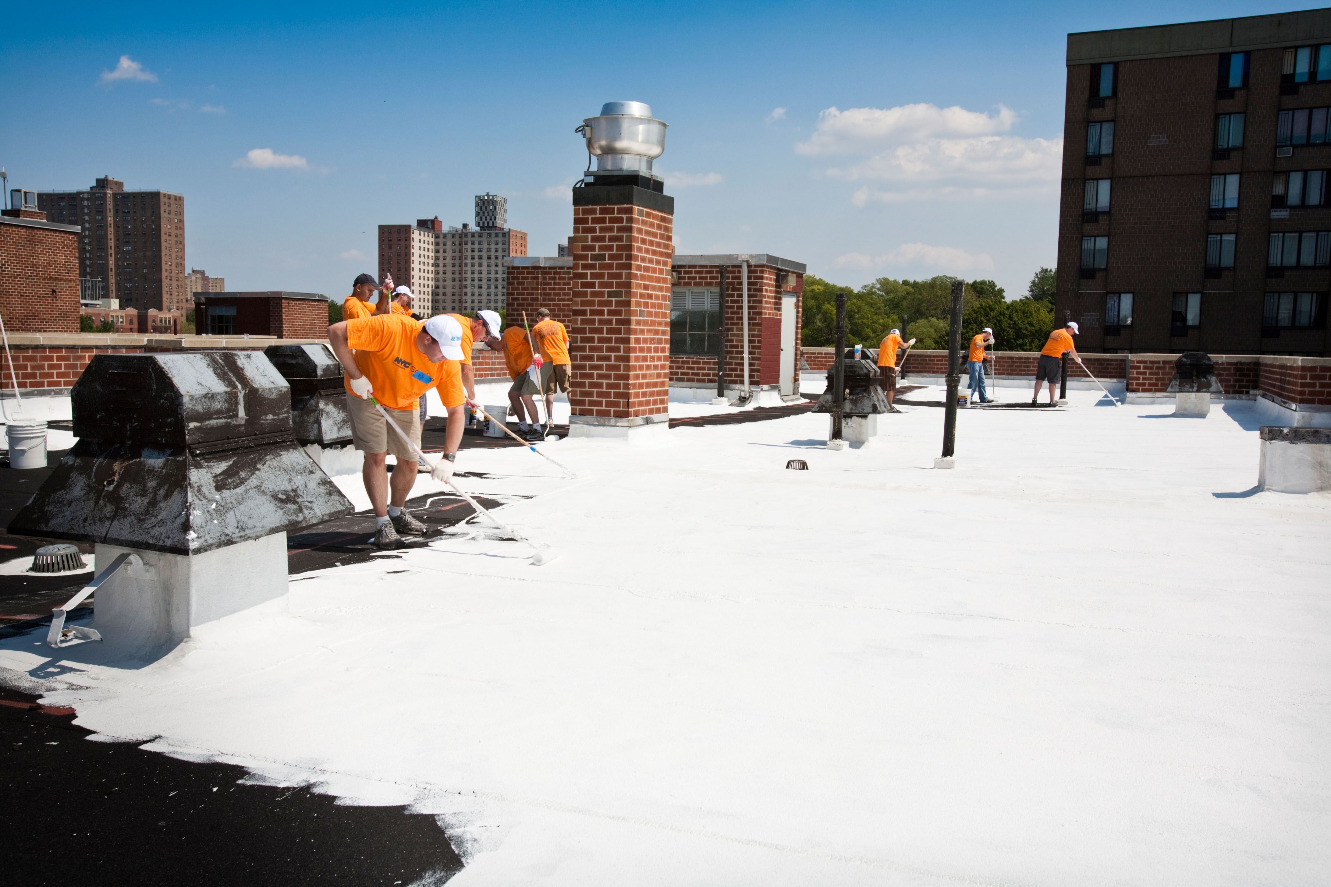 People in hi-vis jackets paint a flat roof with white, reflective paint