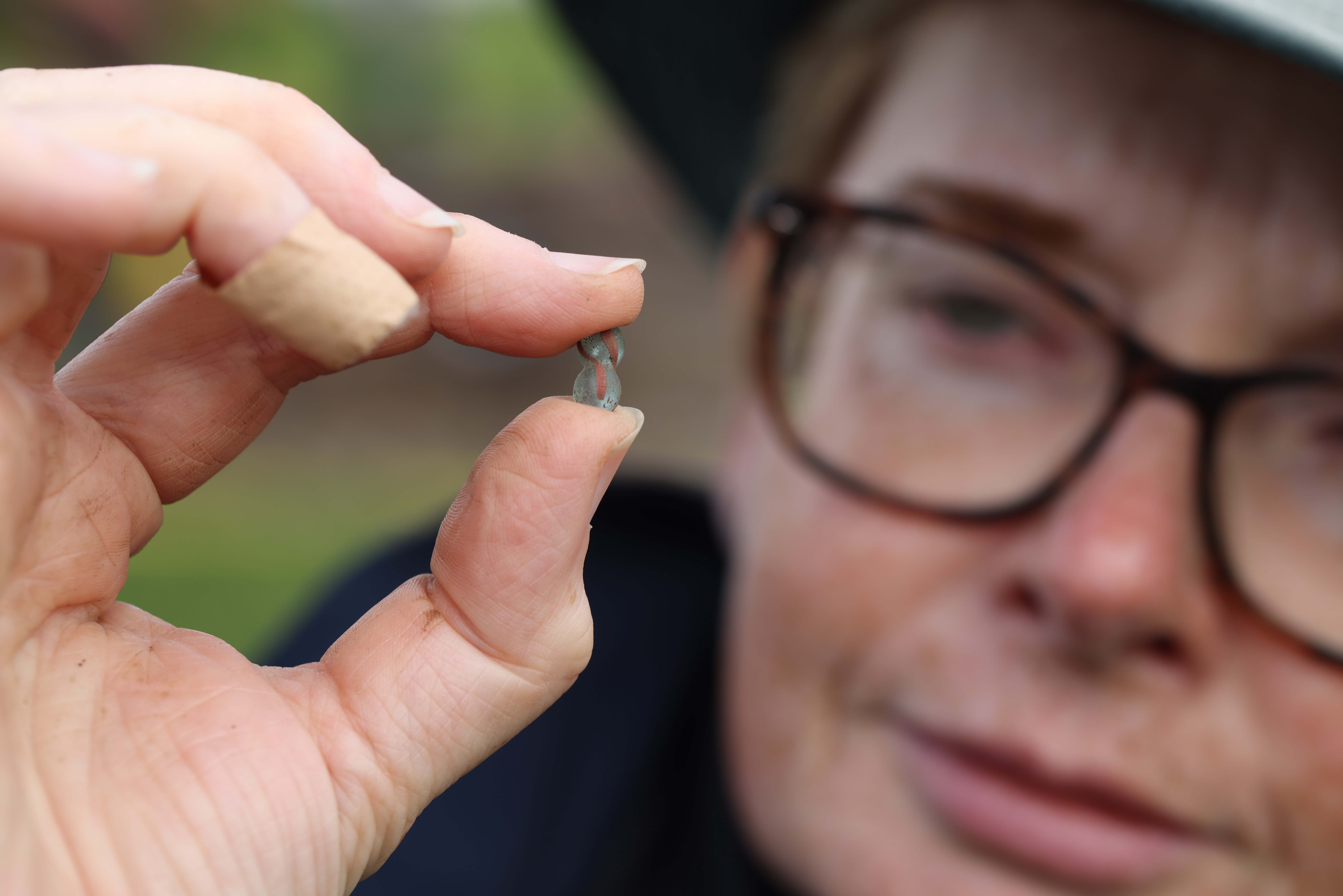 Close up of a turquoise and red glass bead being held by Dr Michelle Comber