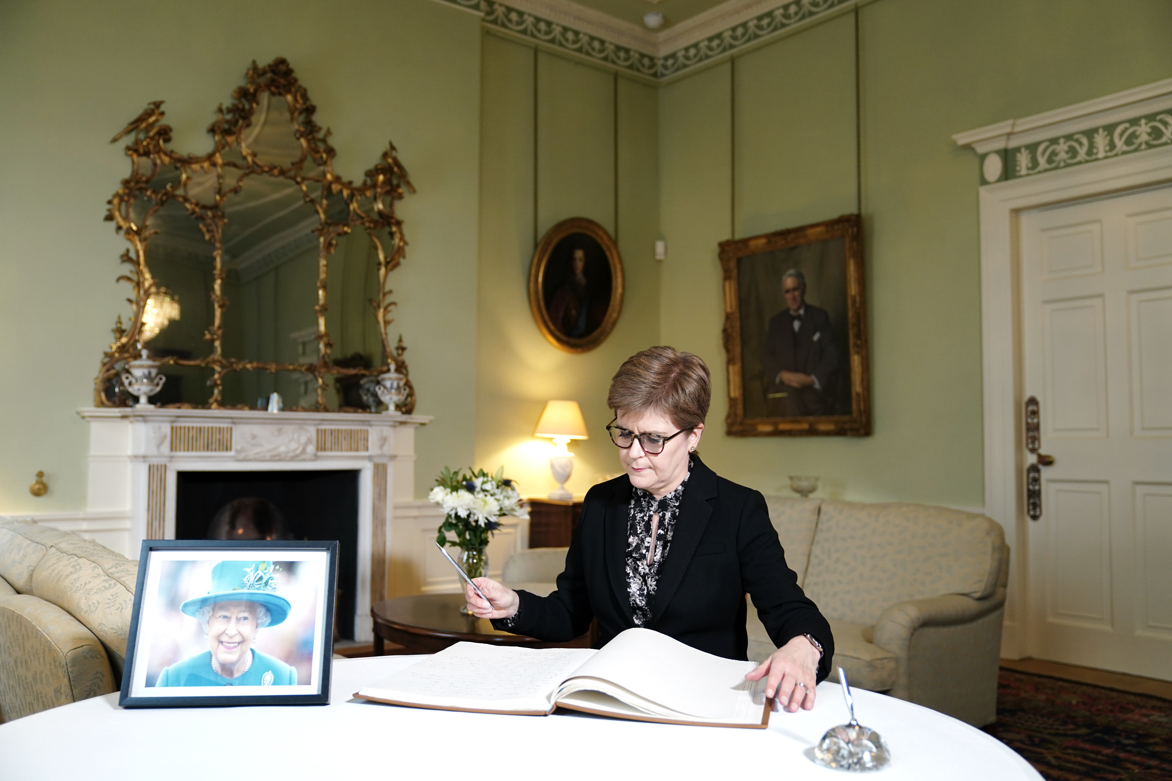 Nicola Sturgeon signing a book of condolence, with a photo of the late Queen beside her